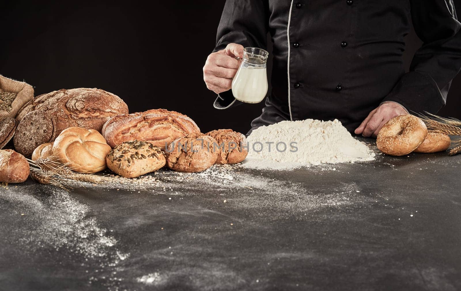 Specialist baker pouring milk into a heap of flour as he prepares the dough for his gourmet bread displayed alongside