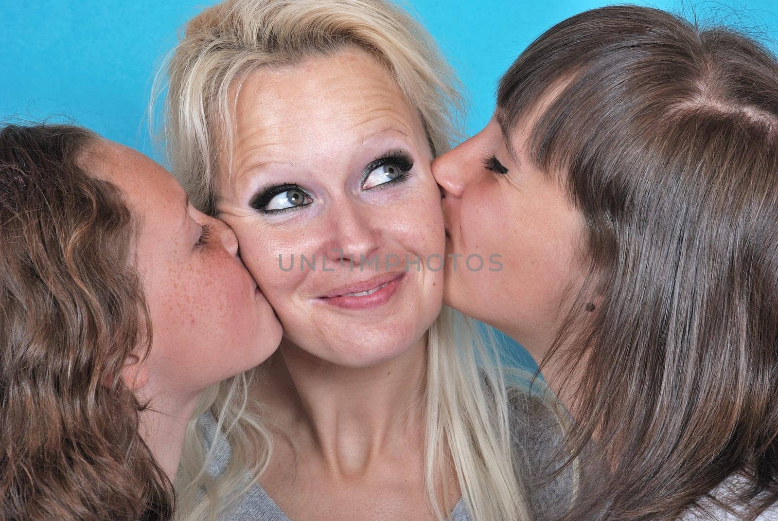 A mother smiles as she receives a kiss on the cheek from her young daughters
