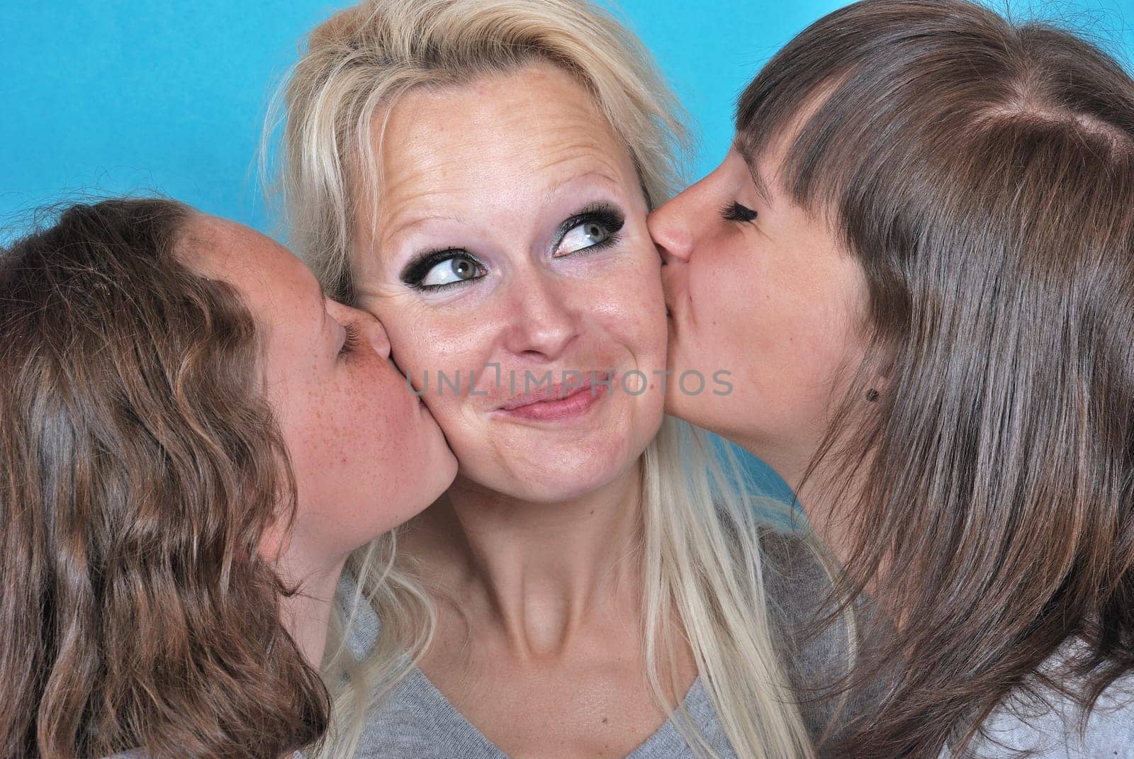 A mother smiles as she receives a kiss on the cheek from her young daughters