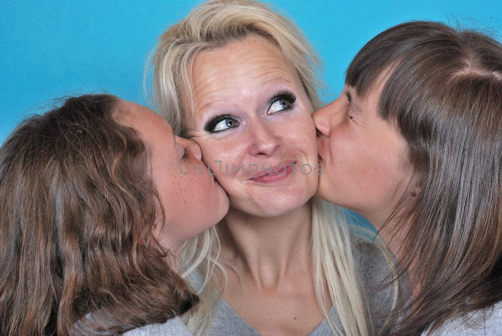 A mother smiles as she receives a kiss on the cheek from her young daughters