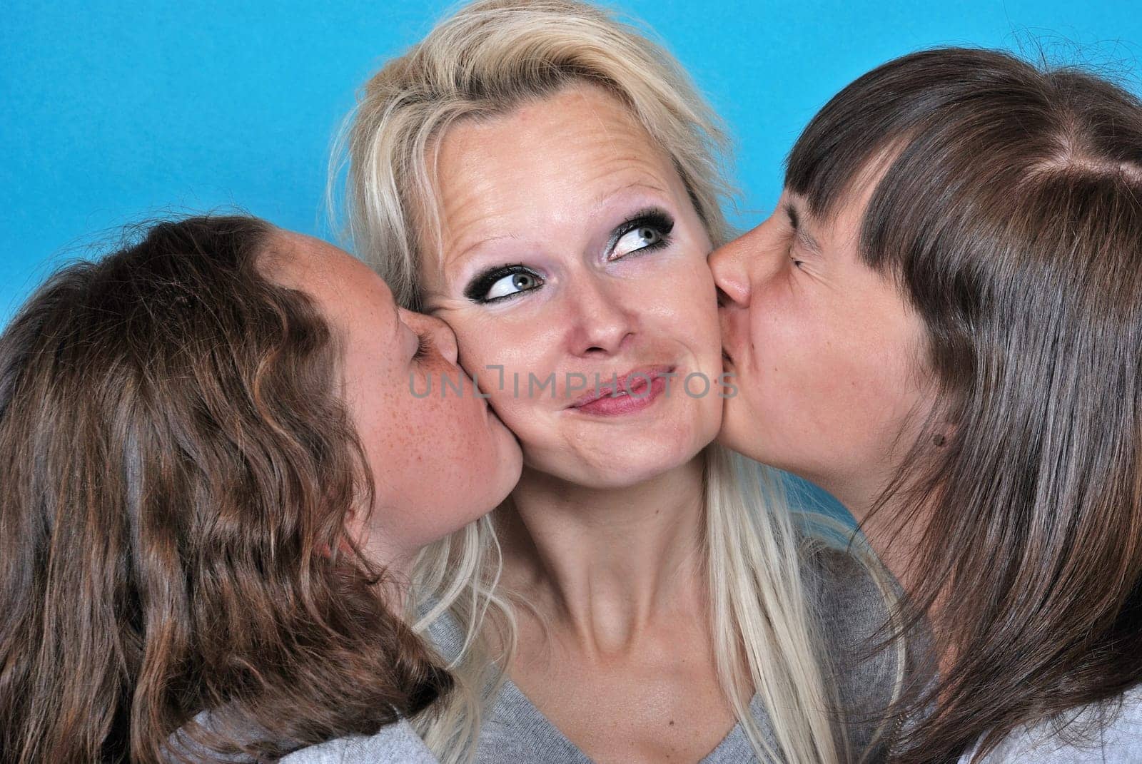 A mother smiles as she receives a kiss on the cheek from her young daughters