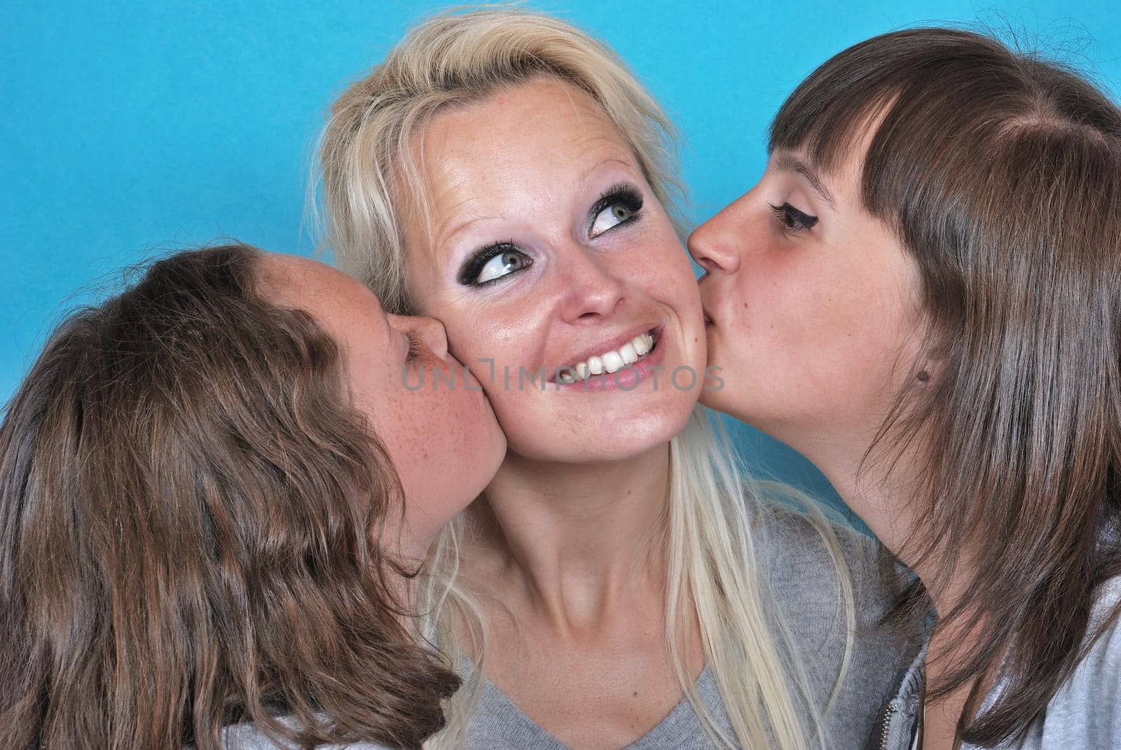A mother smiles as she receives a kiss on the cheek from her young daughters