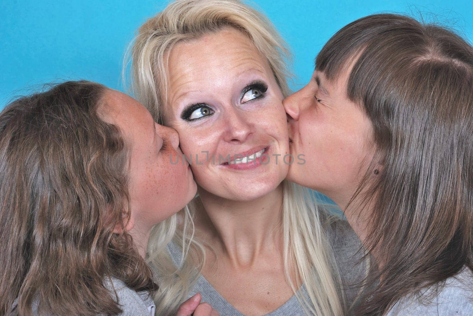 A mother smiles as she receives a kiss on the cheek from her young daughters