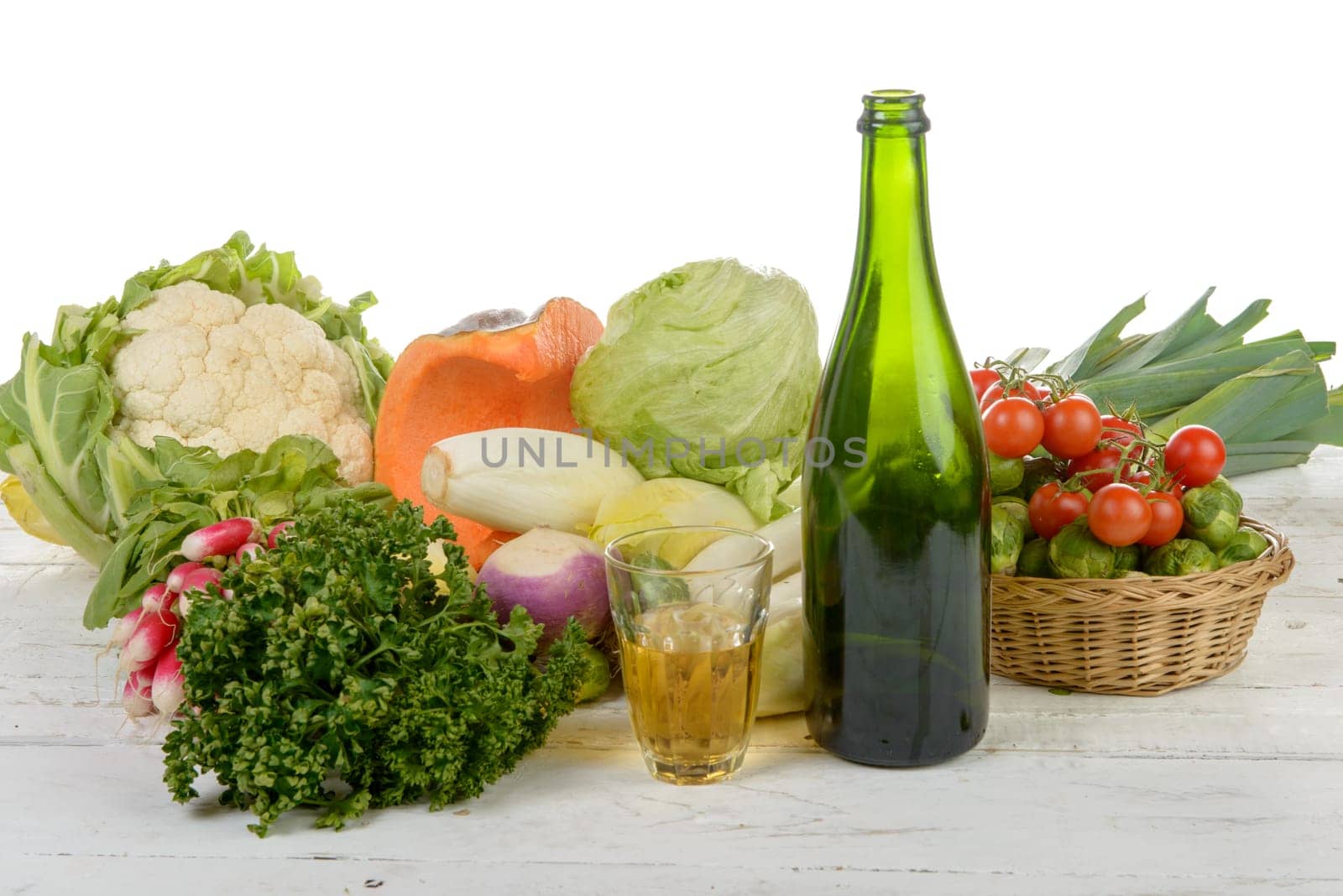 Glass and bottle of cider with vegetables on table