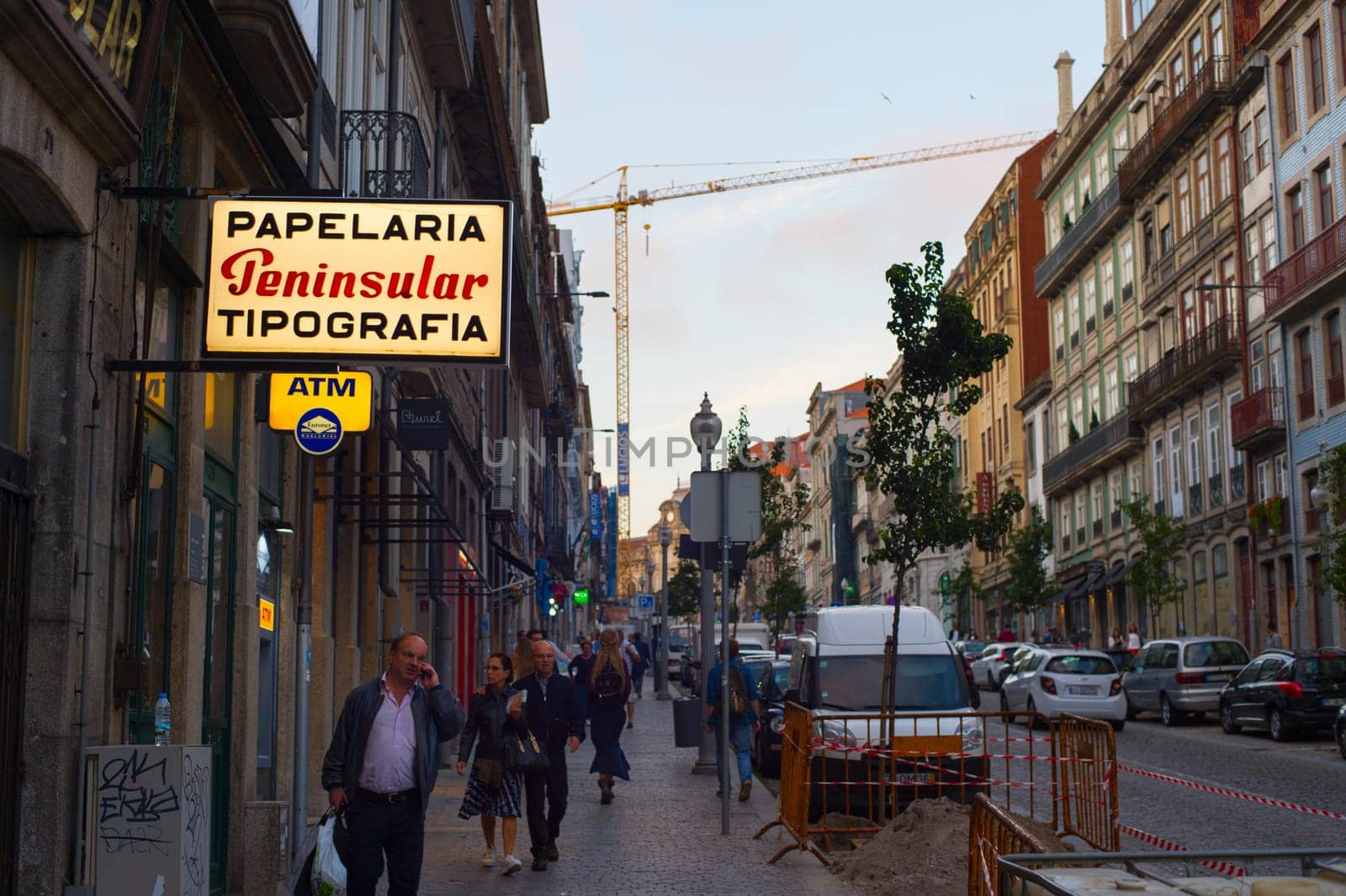 PORTO, PORTUGAL - JUNE 2, 2017: People walking by Porto Old Town street passing atm and typography, building crane in background