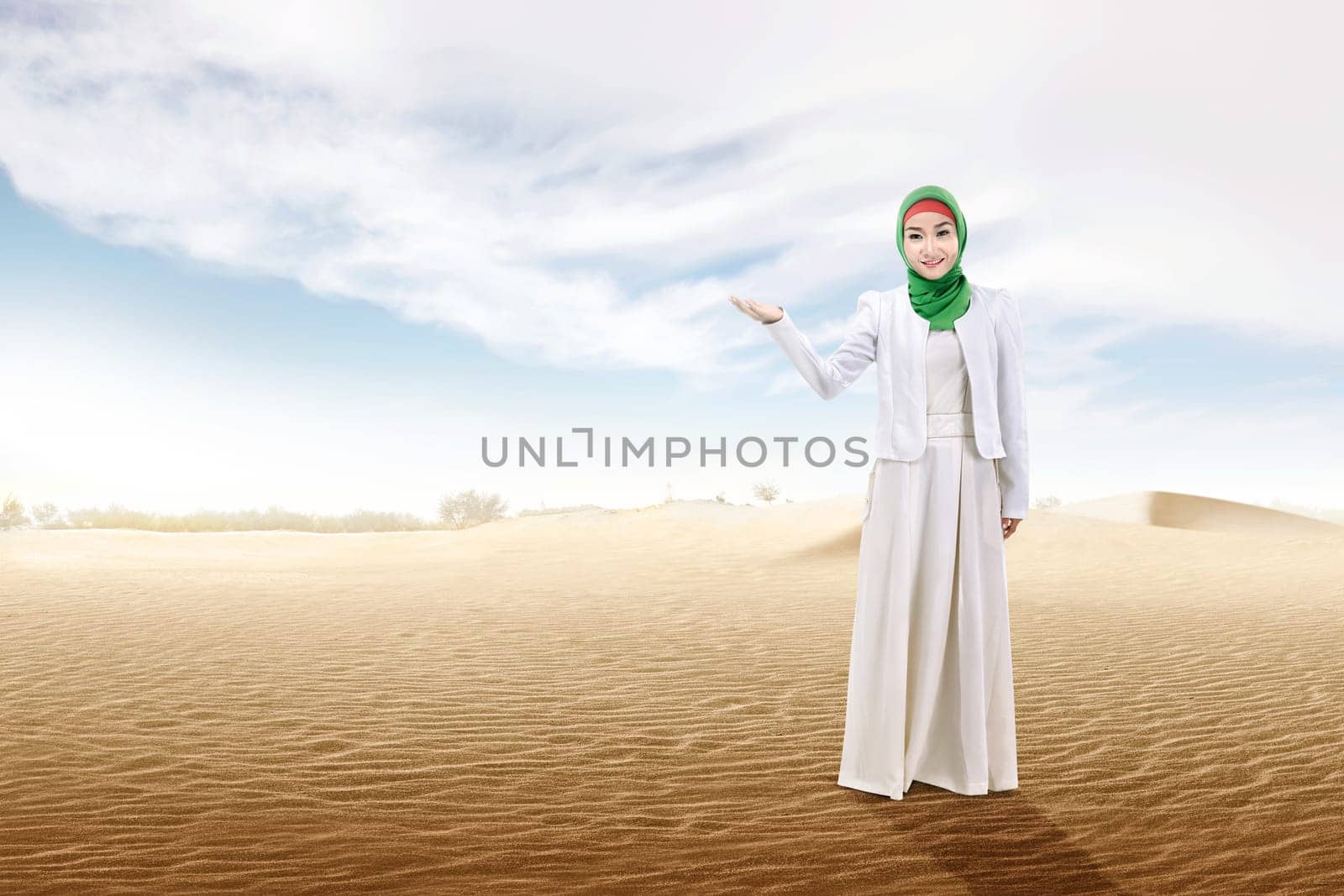 Pretty asian muslim woman with open palm showing something on the sand dune with blue sky background