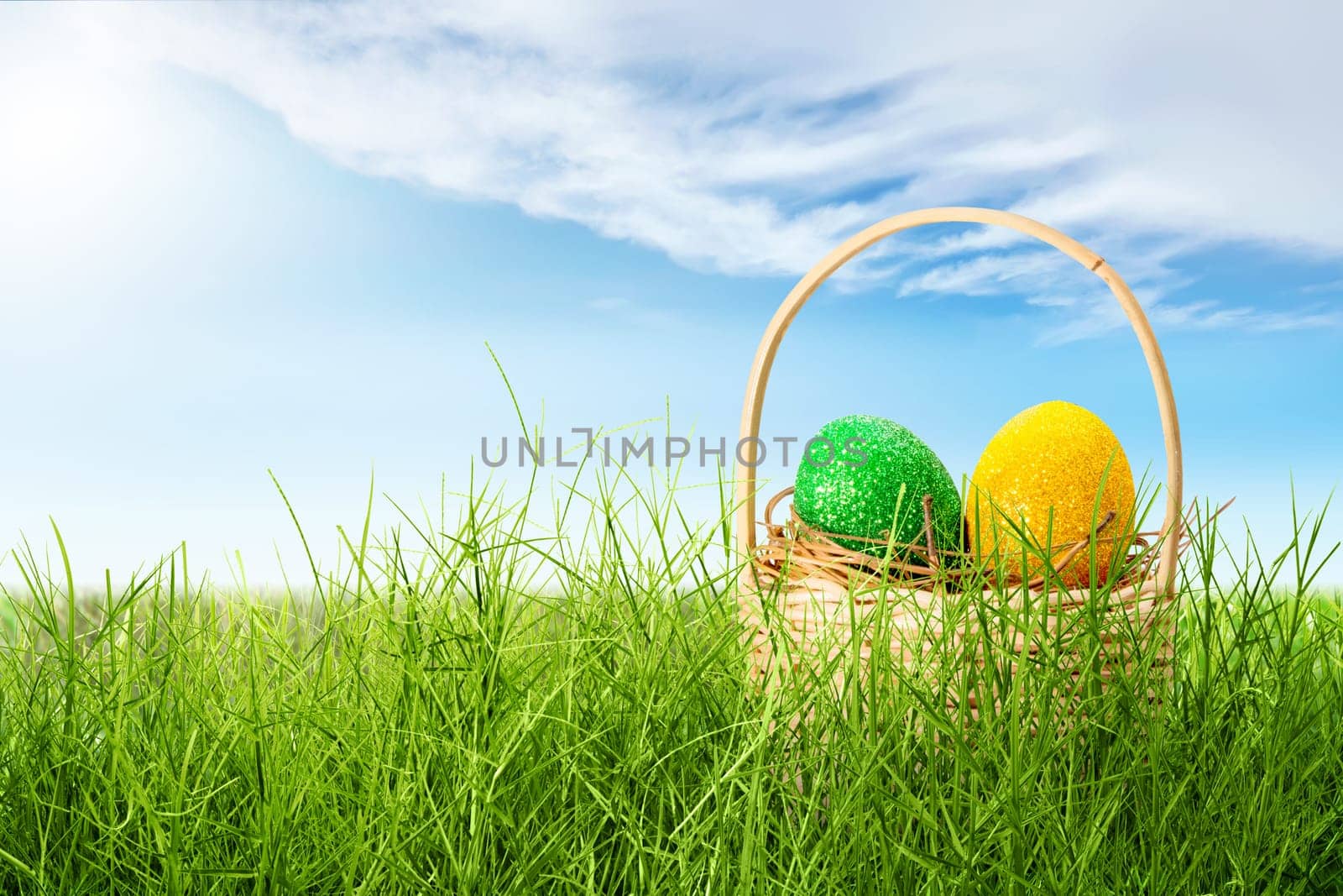 Colorful easter eggs in the nest on wooden basket on the grass field with sunlight and blue sky background. Happy Easter