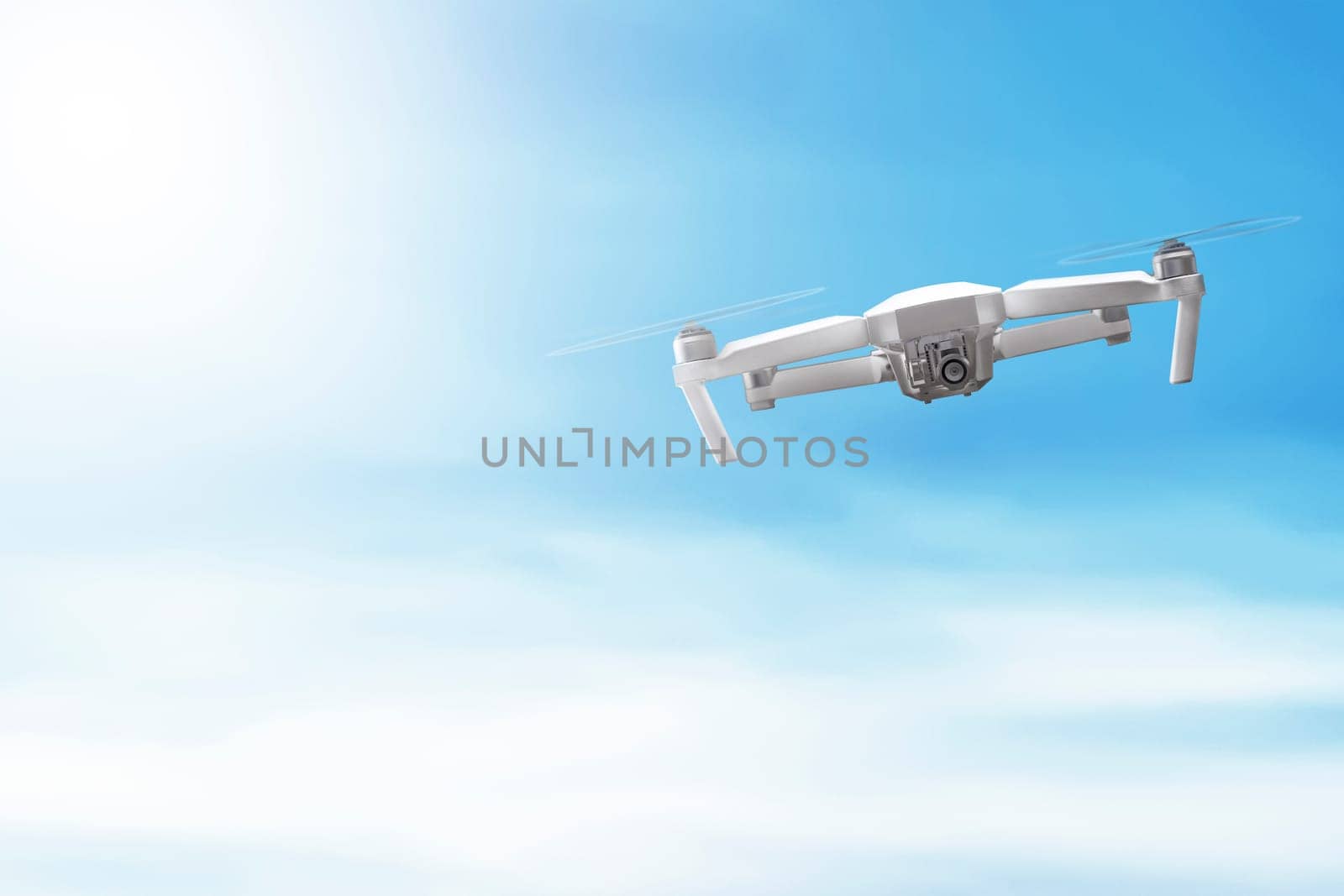White drone with camera flying over blue sky background