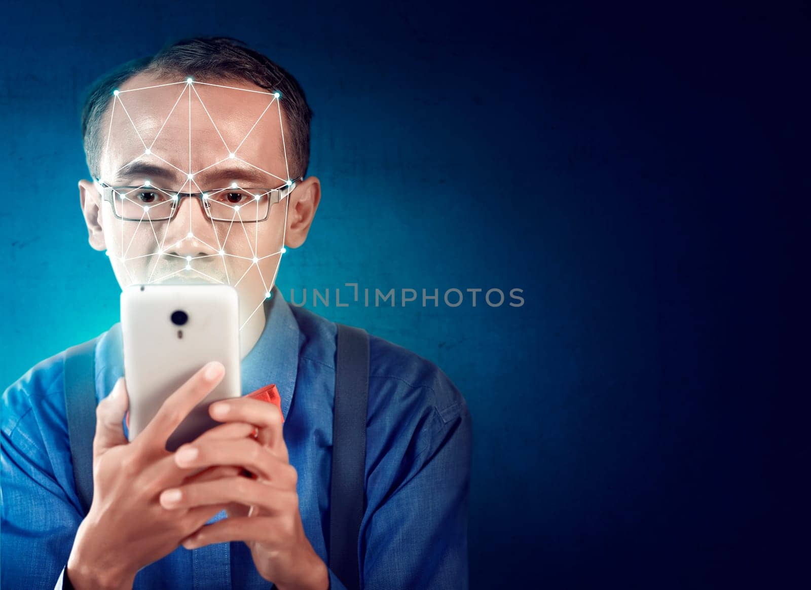 Attractive asian businessman with mobile phone using face recognition over blue background. Modern technology concept
