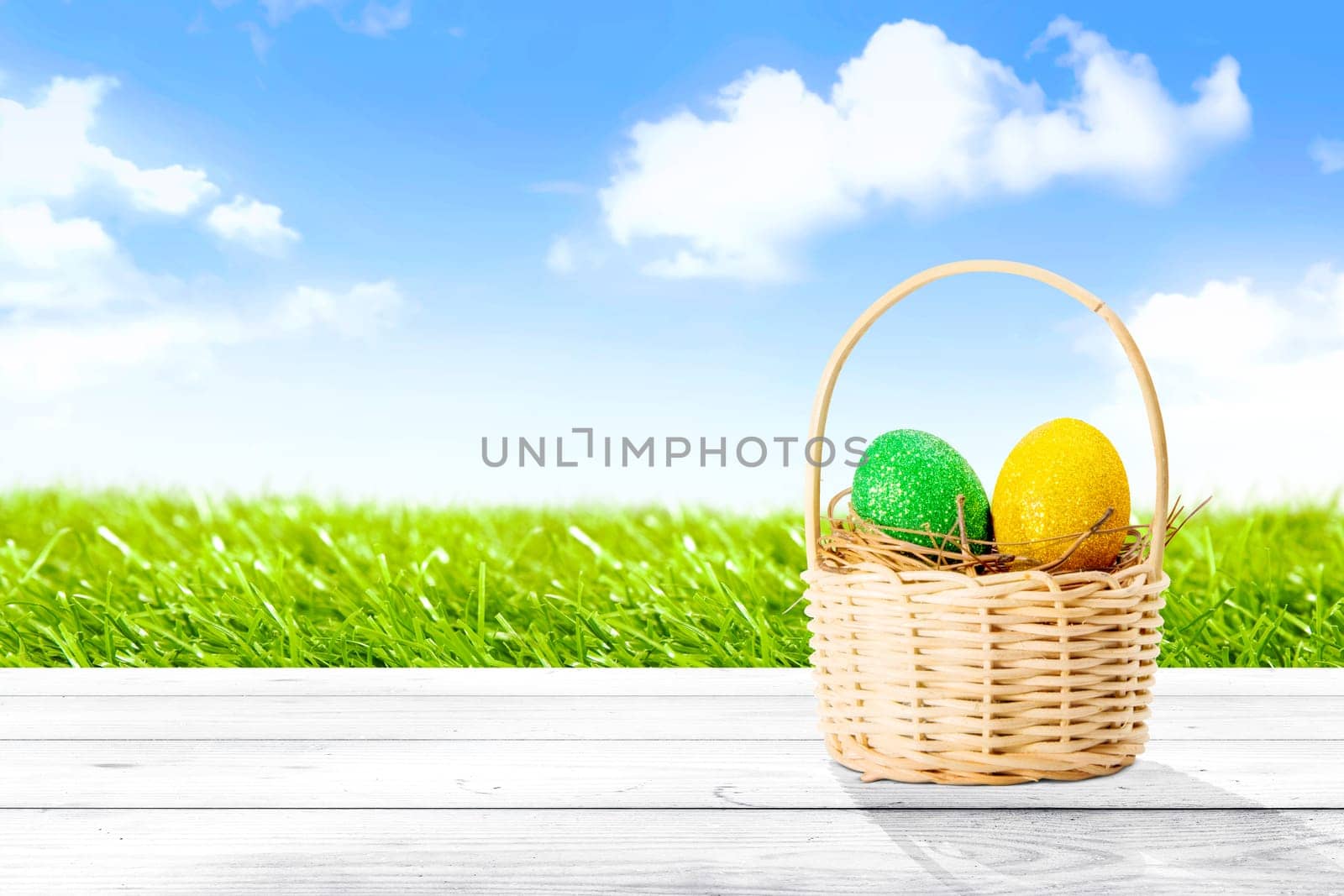 Colorful easter eggs in the nest on wooden basket on wooden table with grass field and blue sky background. Happy Easter