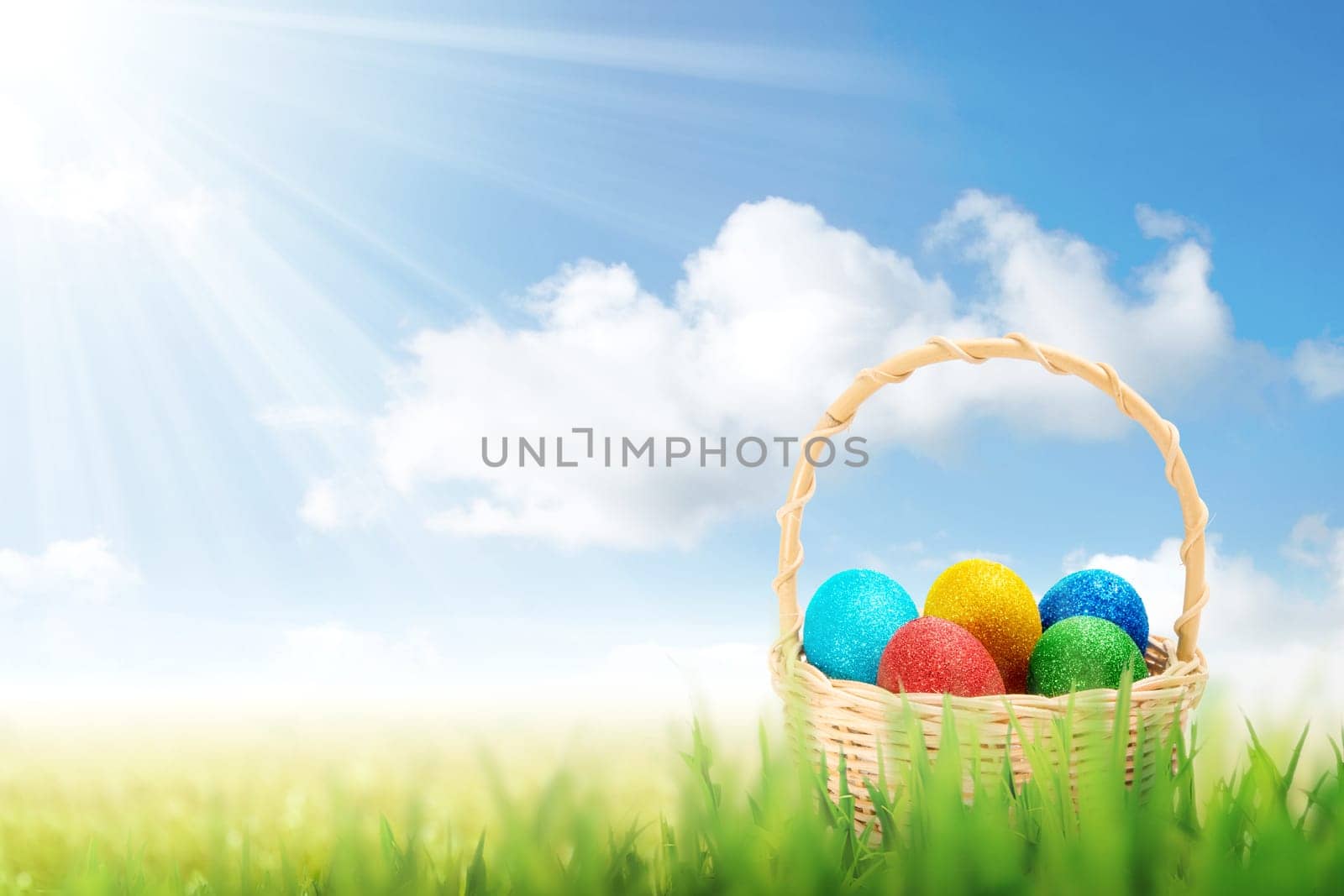 Colorful easter eggs in wooden basket on the grass field with sunlight and blue sky background. Happy Easter