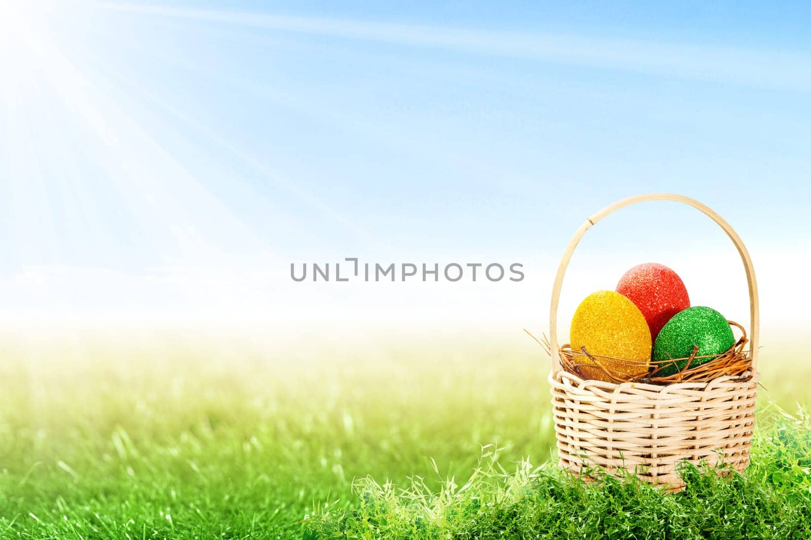Colorful easter eggs in the nest on wooden basket on the grass field with sunlight and blue sky background. Happy Easter