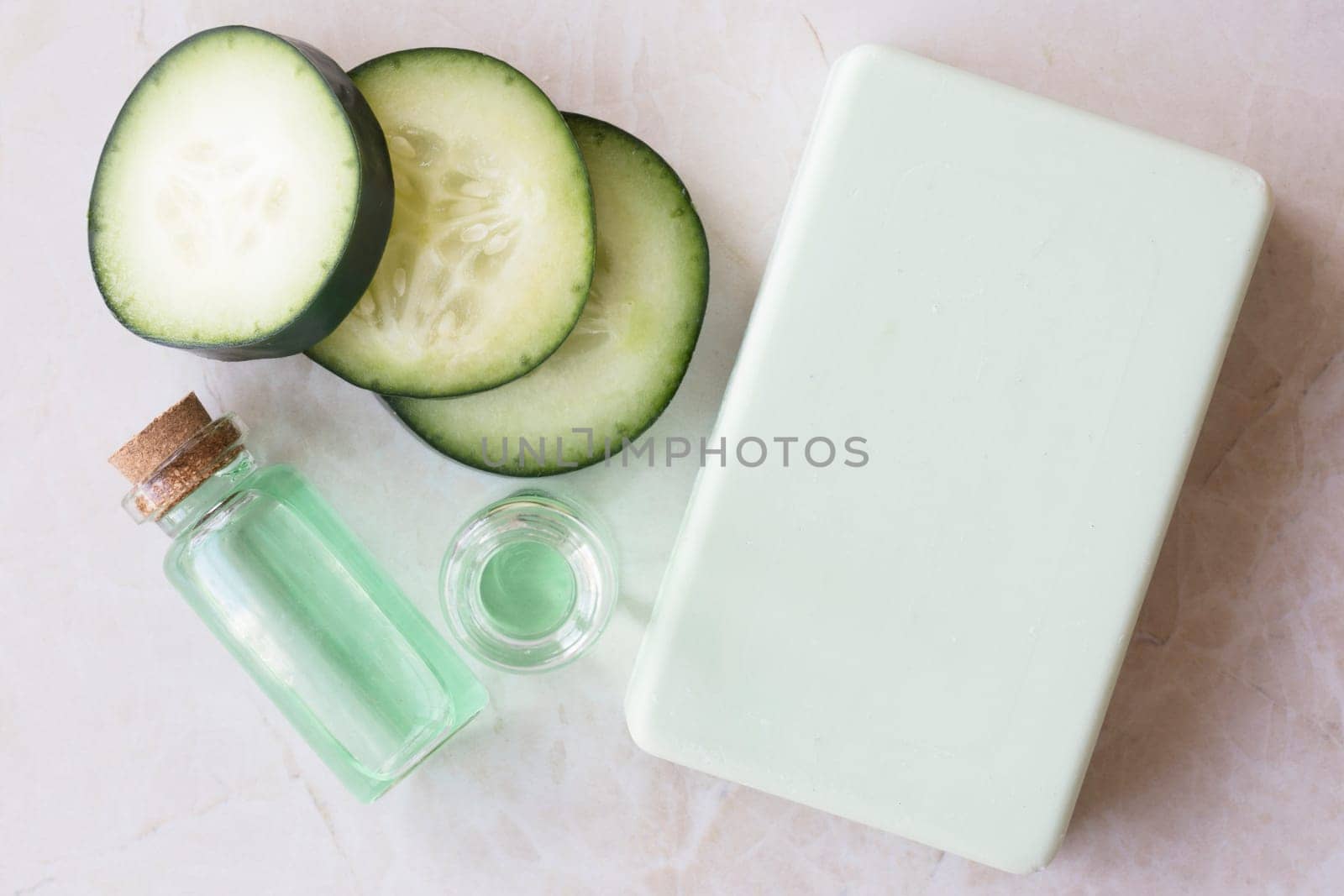 Cucumber extract in small bottle with bar of soap and cucumber slices flat lay