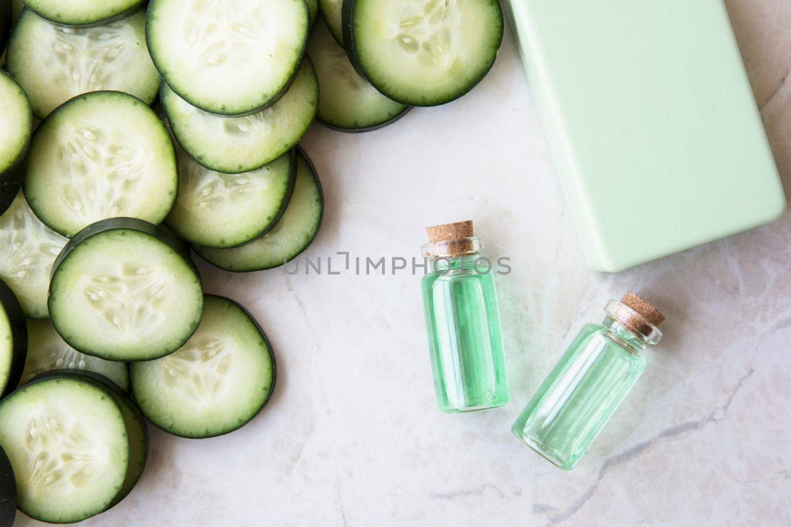Cucumber extract in small bottle with bar of soap and cucumber slices flat lay