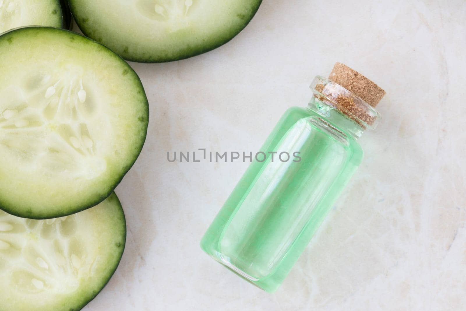 Cucumber slices and small bottle of cucumber extract flat lay.