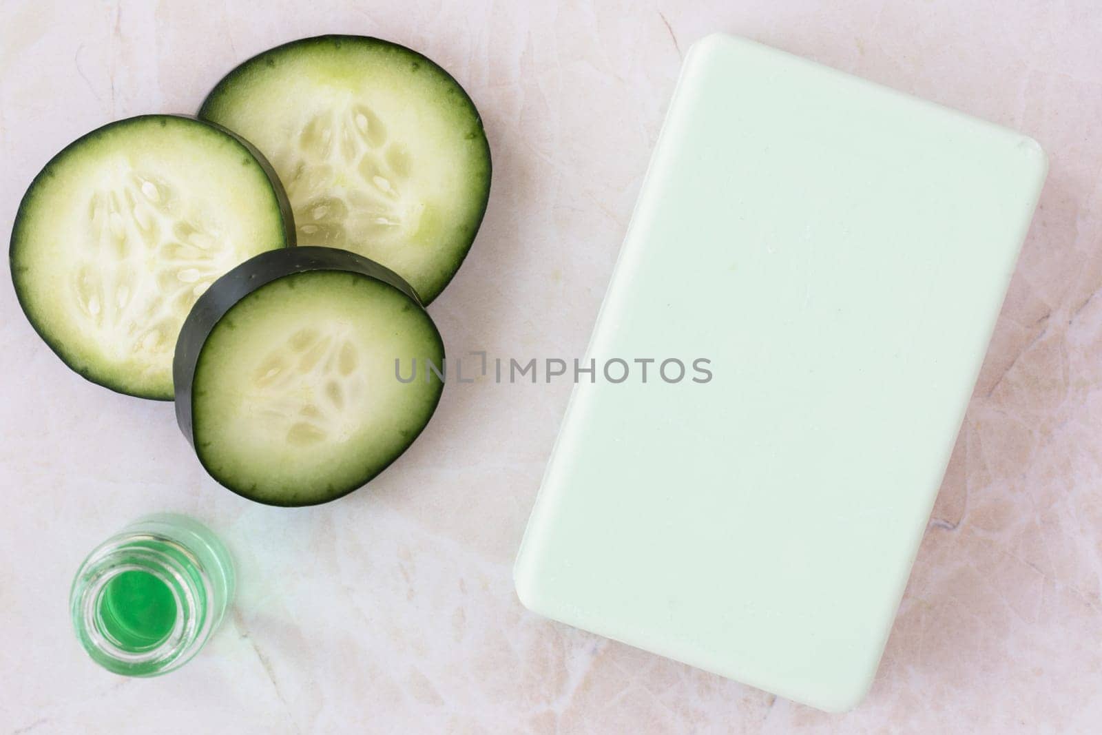Cucumber extract in small bottle with bar of soap and cucumber slices flat lay
