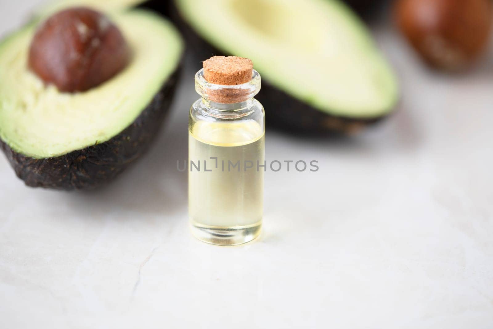 Small bottle of avocado oil and avocados on marble surface