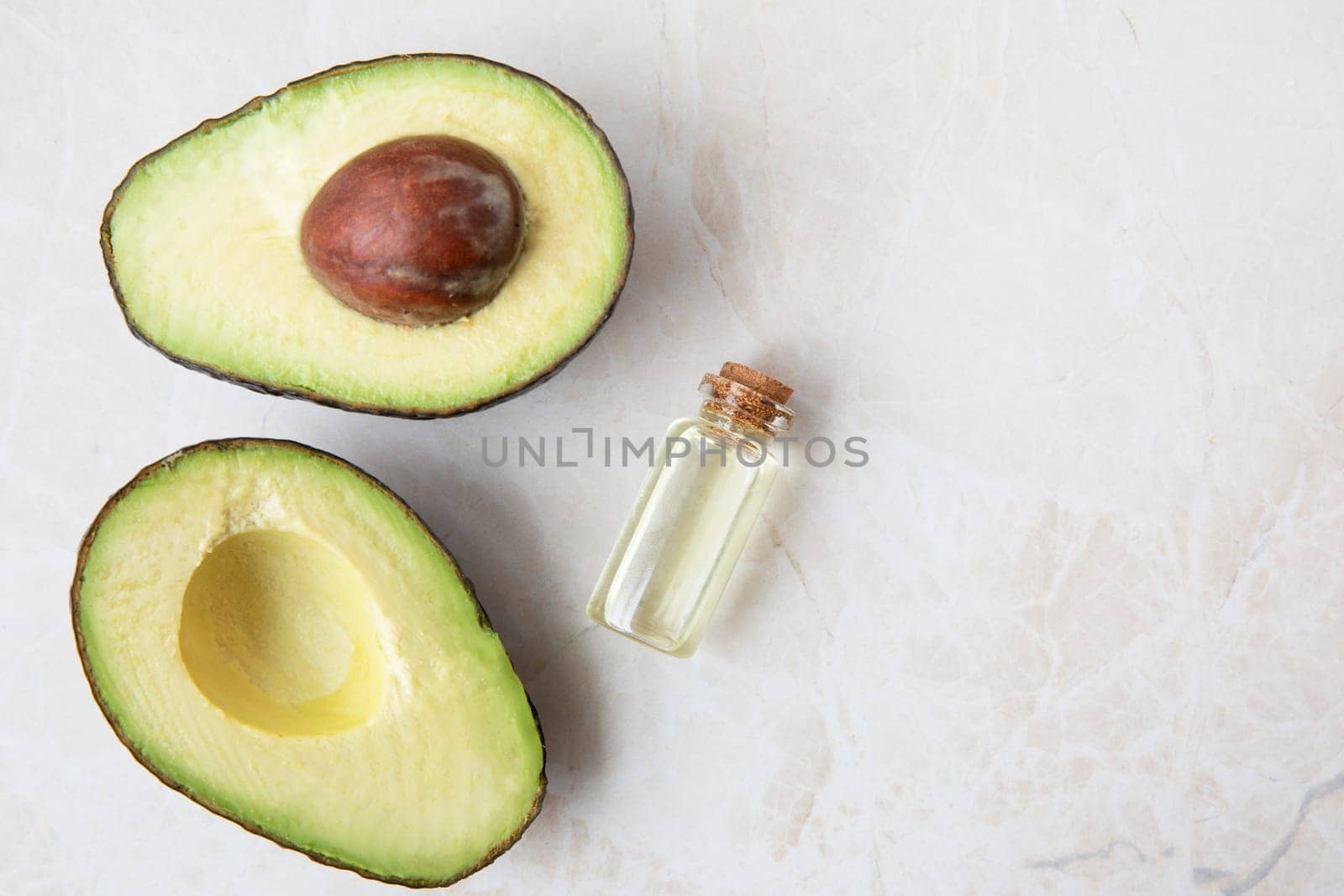 Small bottle of avocado oil and avocados on marble surface