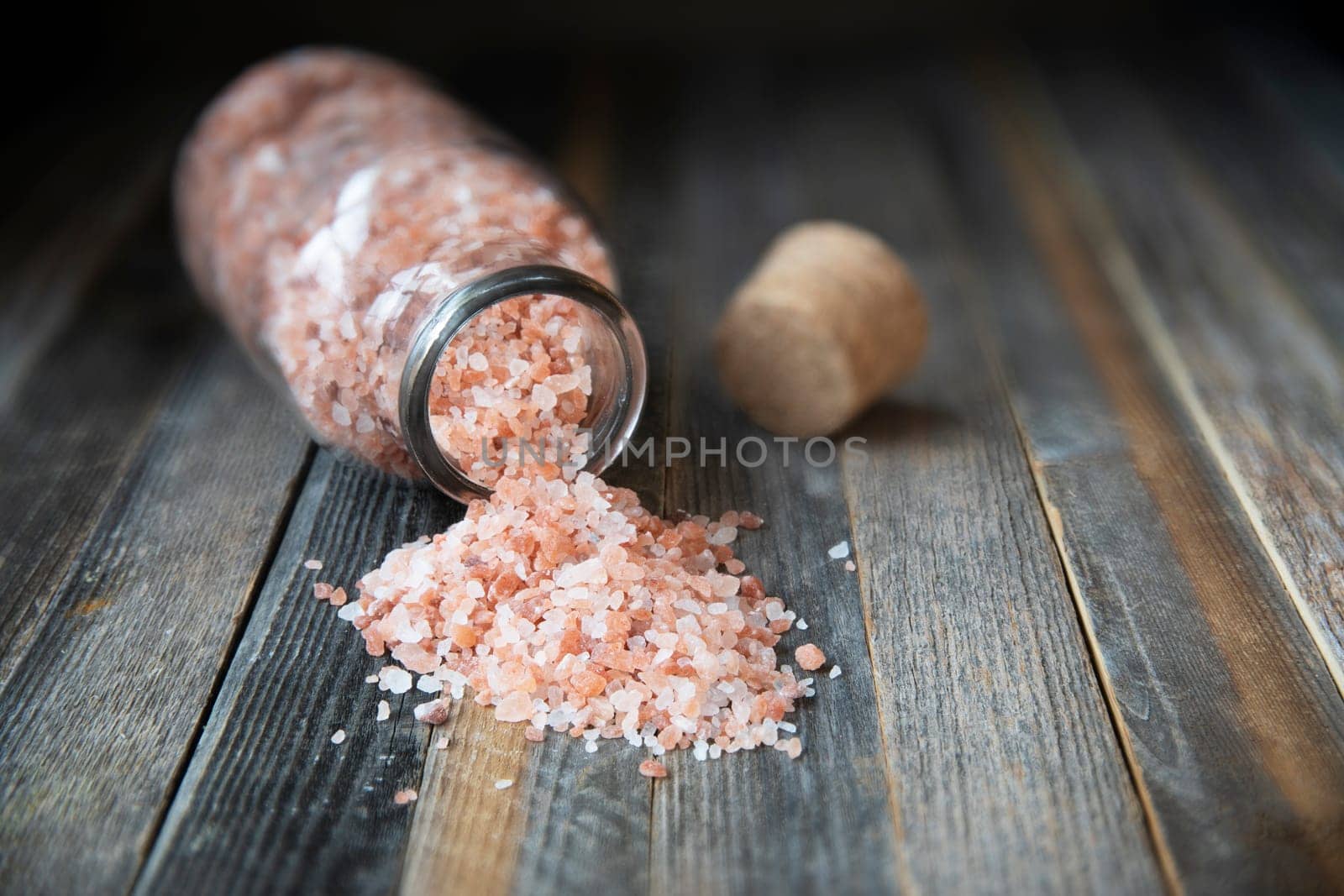 Pink Himalayan salt crystals in glass bottle and small bowl on wooden table.