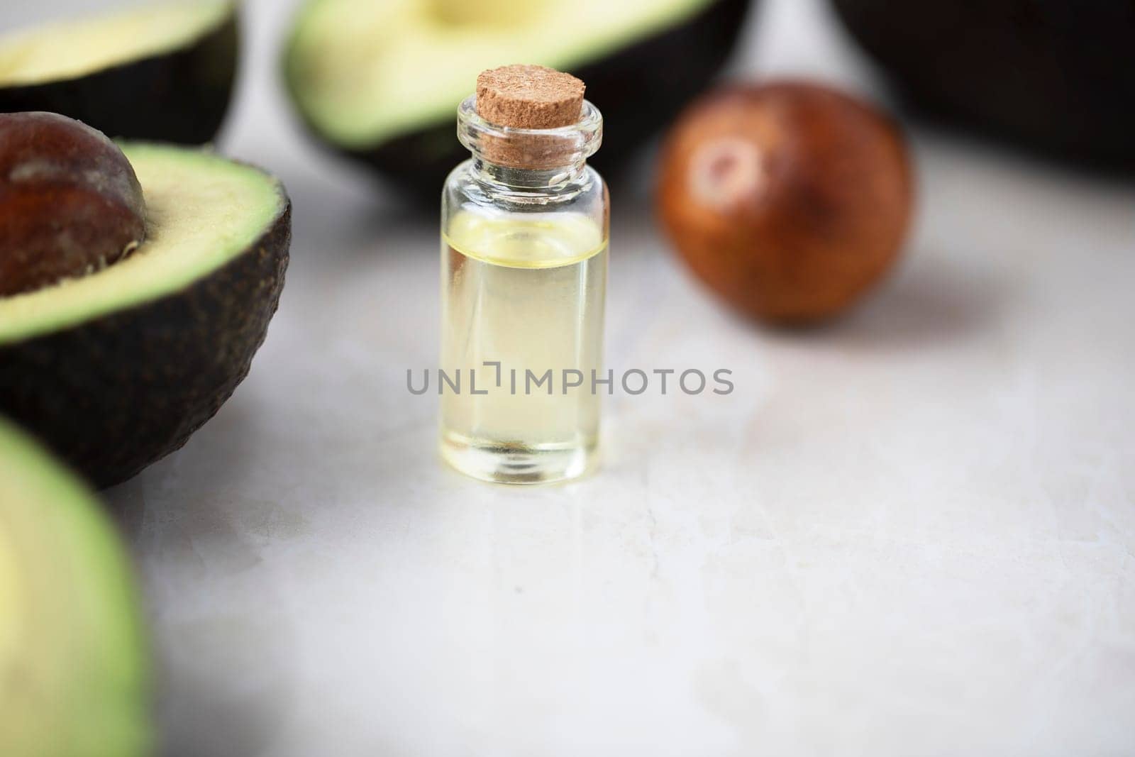 Small bottle of avocado oil and avocados on marble surface