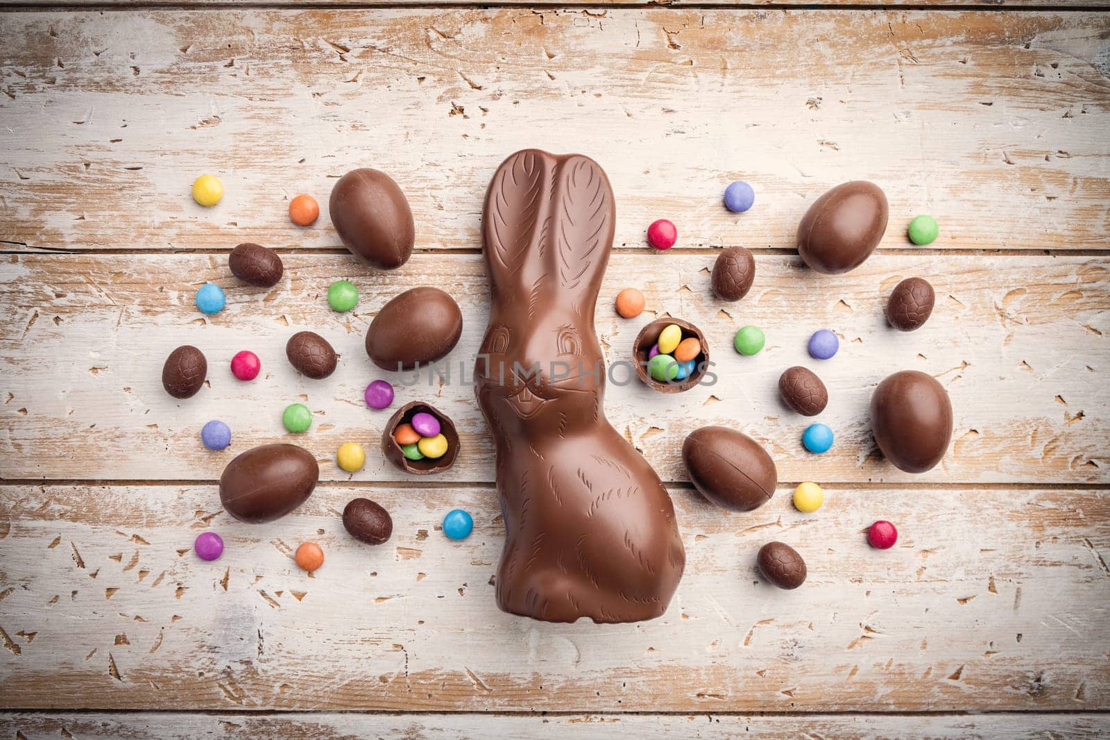Delicious chocolate Easter bunny, eggs and sweets on rustic background