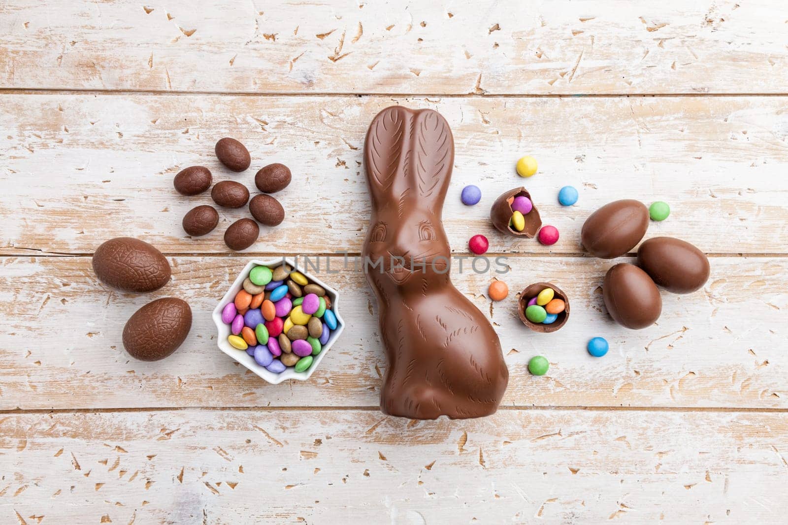 Delicious chocolate Easter bunny, eggs and sweets on rustic background