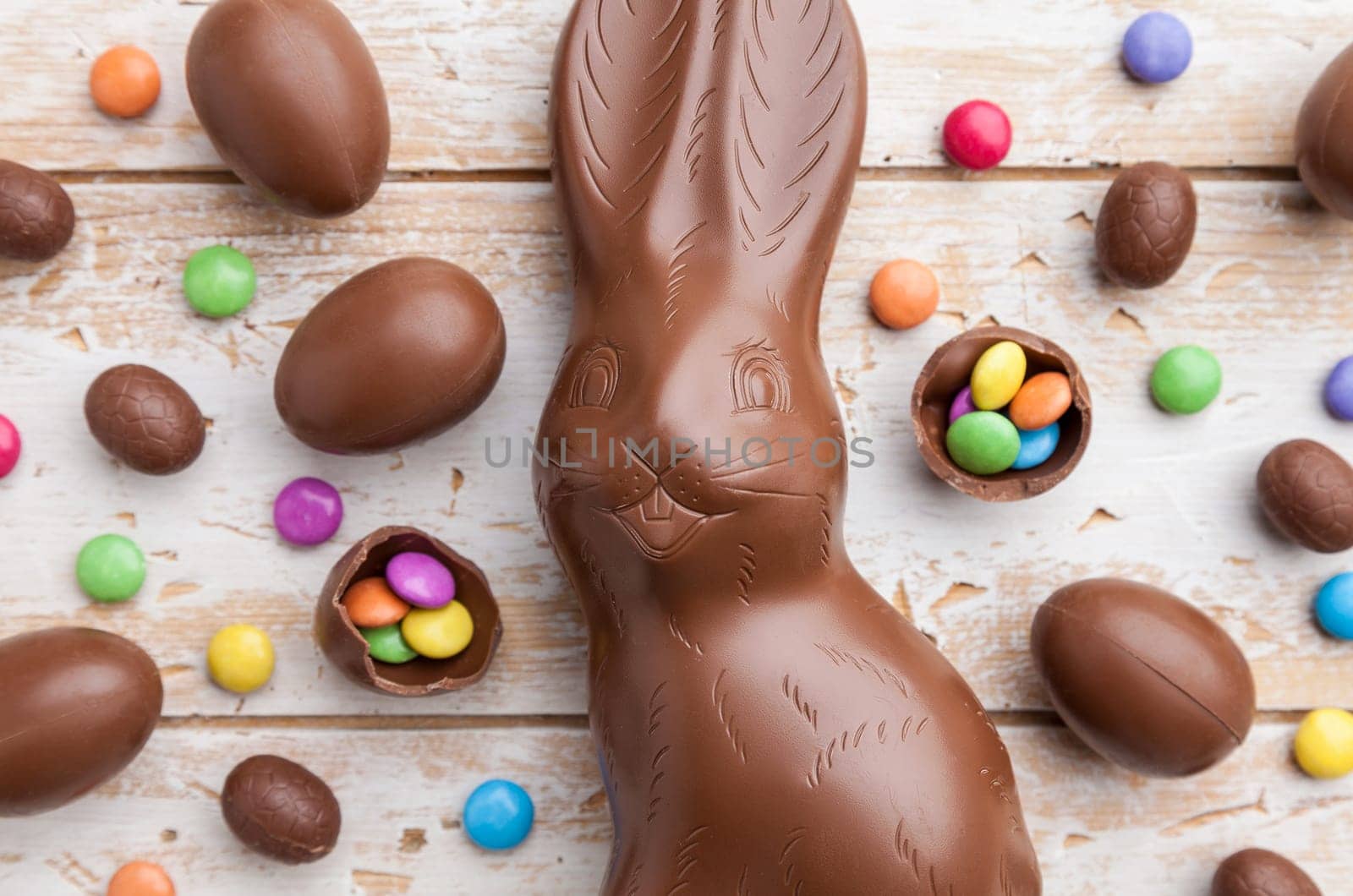 Delicious chocolate Easter bunny, eggs and sweets on rustic background