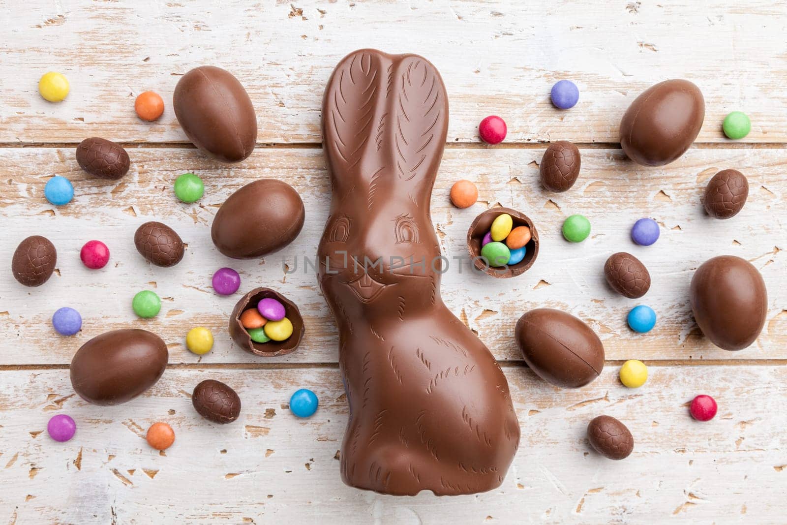Delicious chocolate Easter bunny, eggs and sweets on rustic background