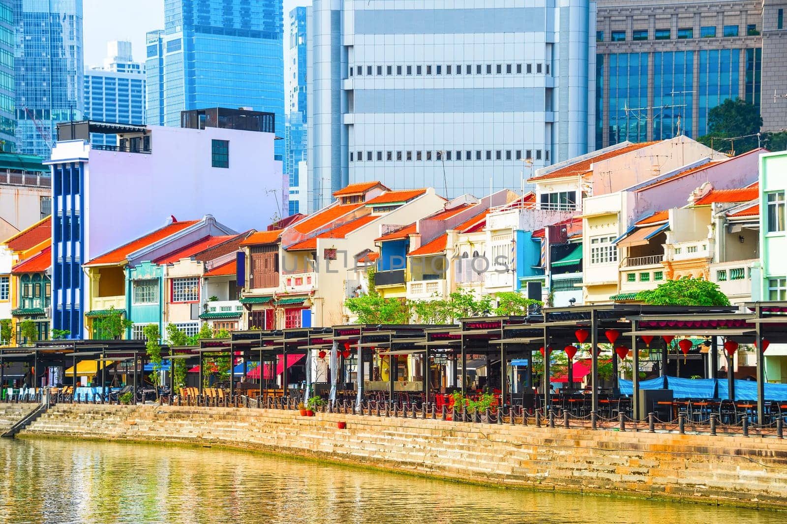Cityscape with colorful bars, restaurants and stores by the Singapore River along Boat Quay, skyscrapers of modern architecture in background