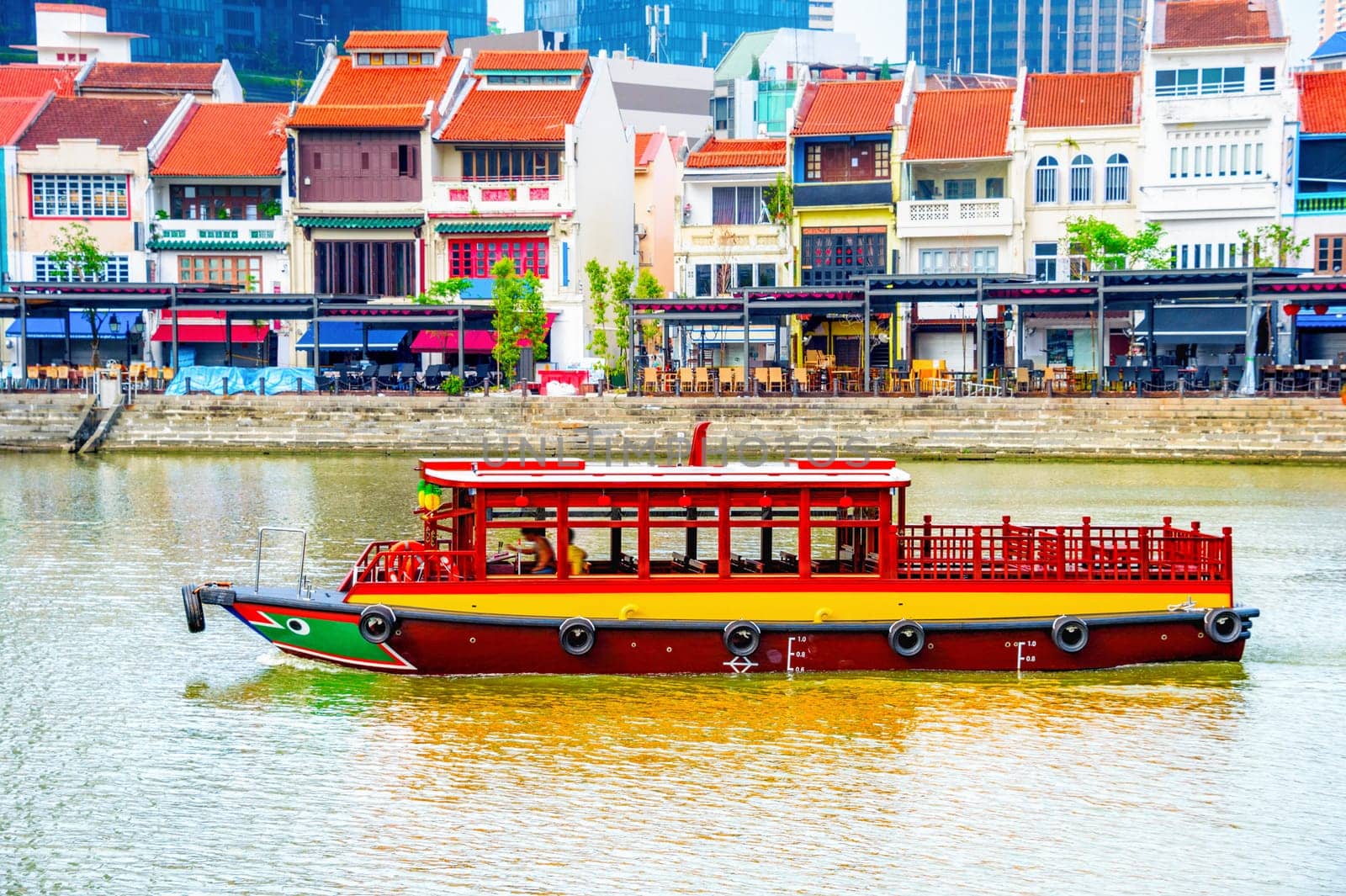 Traditional tourist boat cruising by Boat Quay with colorful restaurants, Singapore cityscape