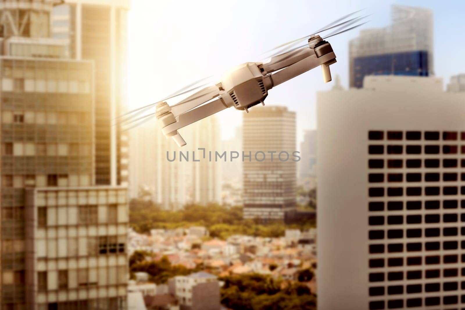 White drone with camera flying above modern city with skyscrapers and sunset view background
