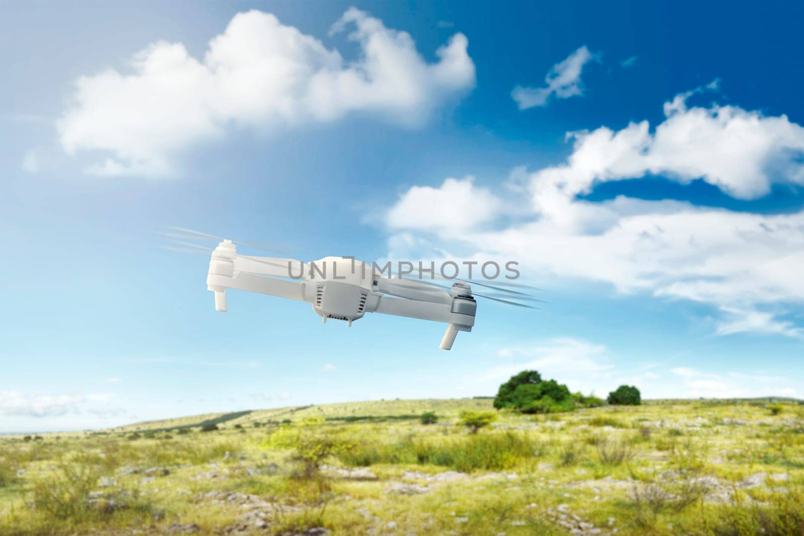 White drone with camera flying above the field with green grass and trees with blue sky background