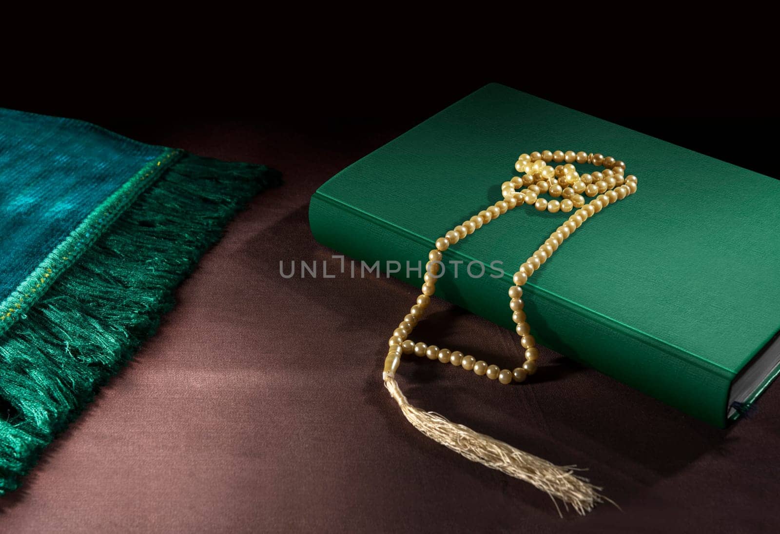 Quran and prayer beads with prayer mat on the floor over black background