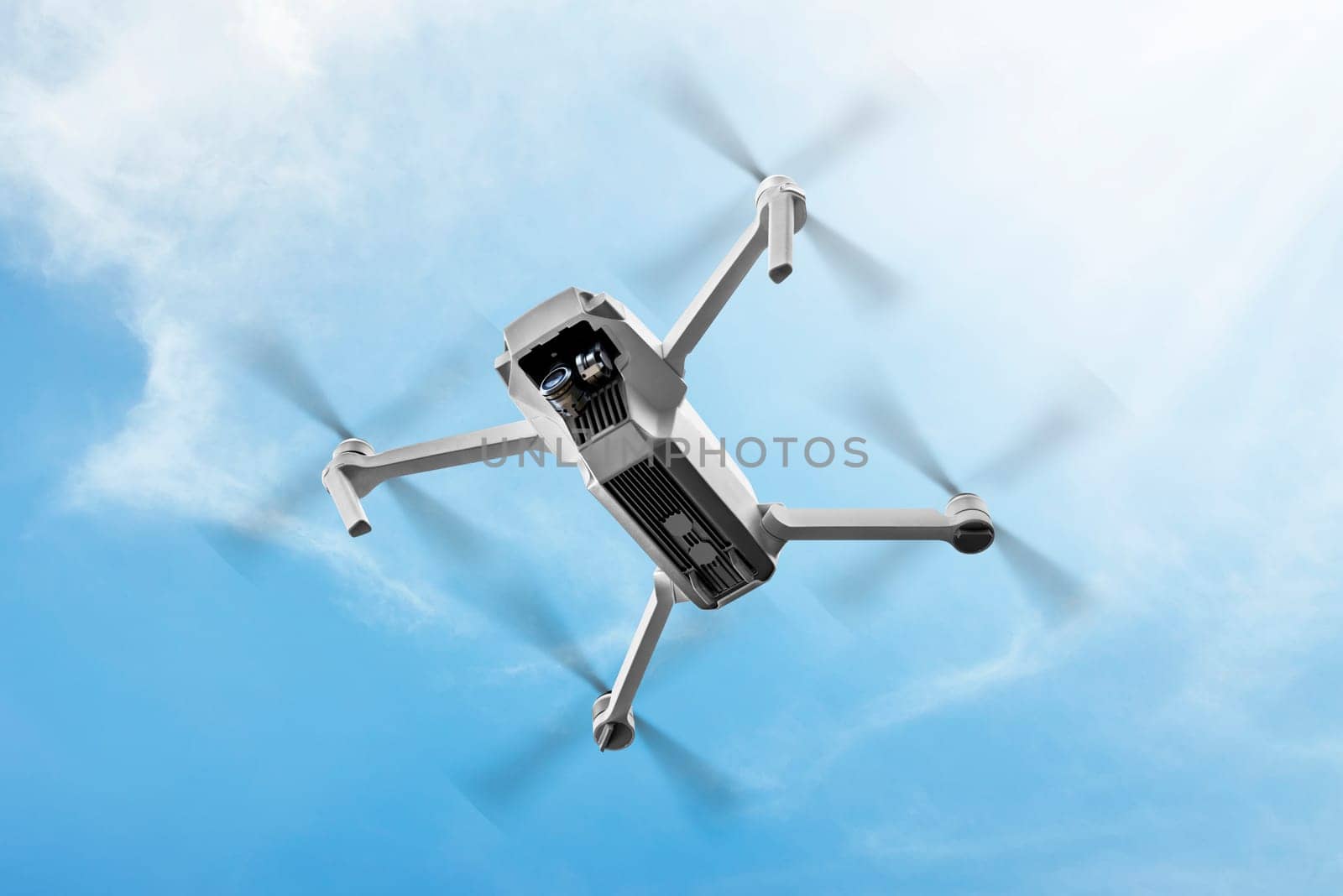 White drone with camera flying in the air over blue sky background