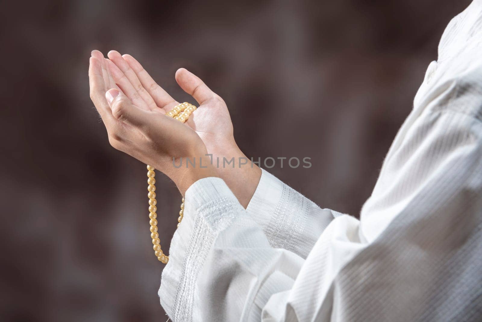 Muslim man praying with prayer beads on his hands over blurry background