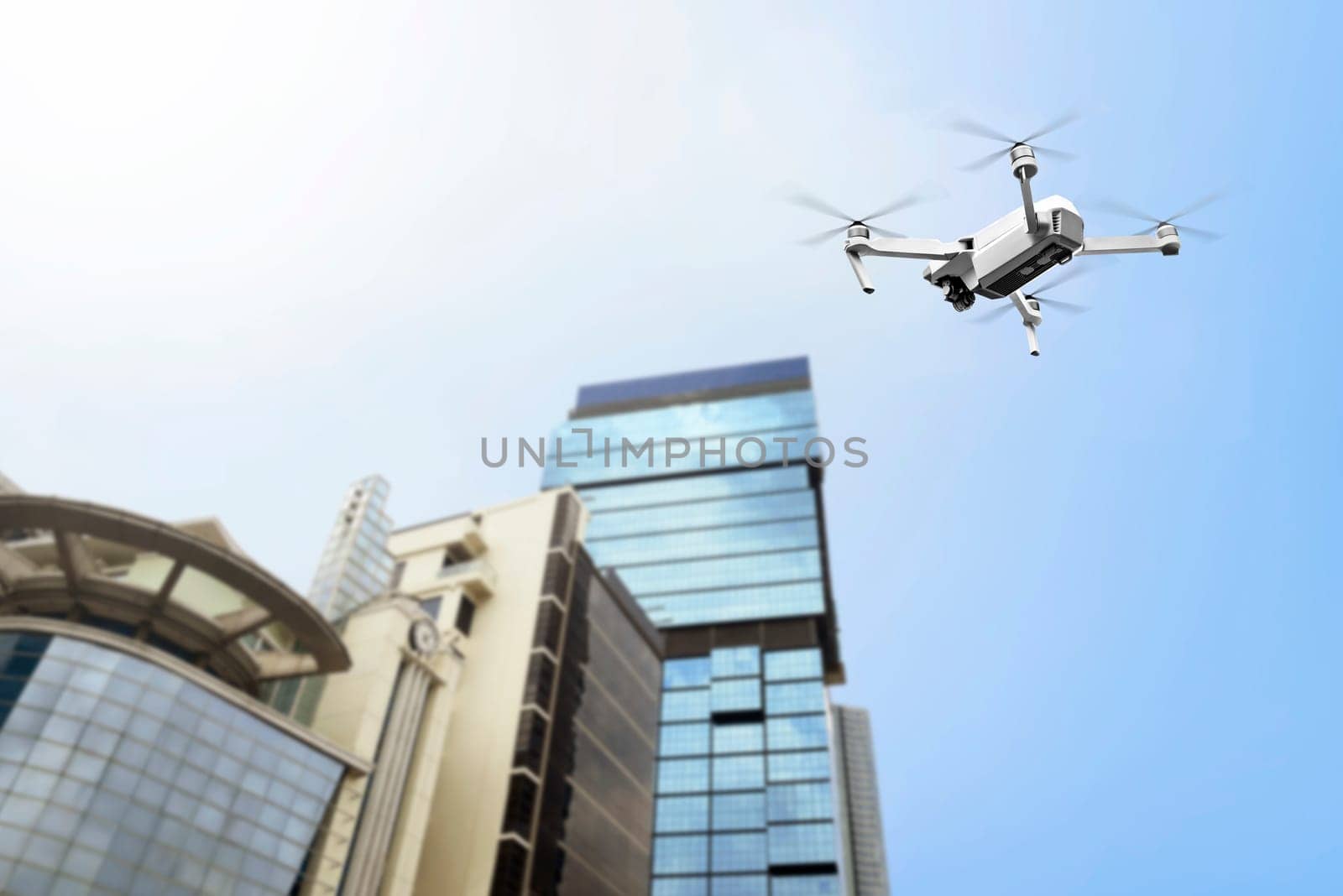 White drone with camera flying to the top of modern building with blue sky background