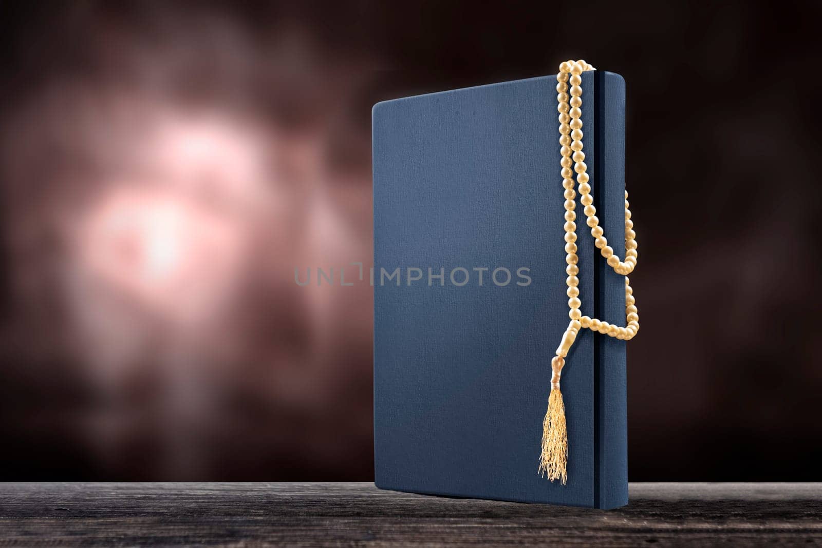 Quran and prayer beads on wooden table over blurry background
