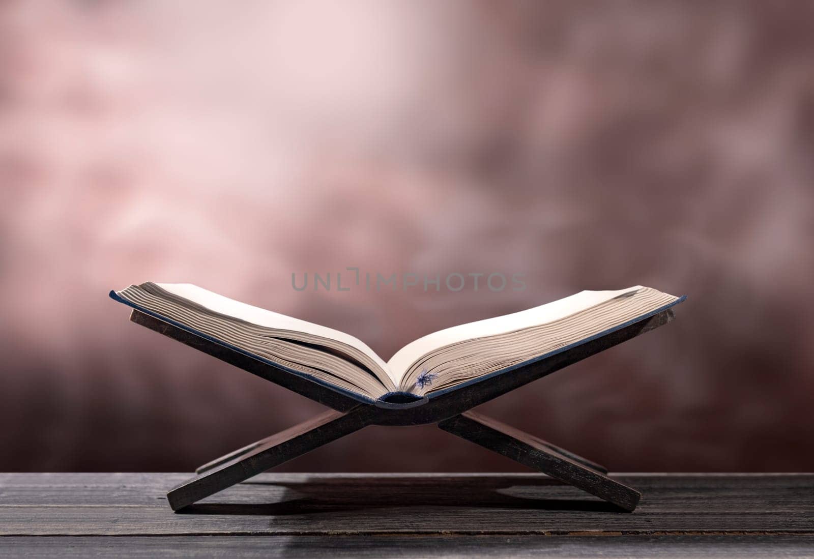 Quran open in wooden placemat on wooden table over blurry background
