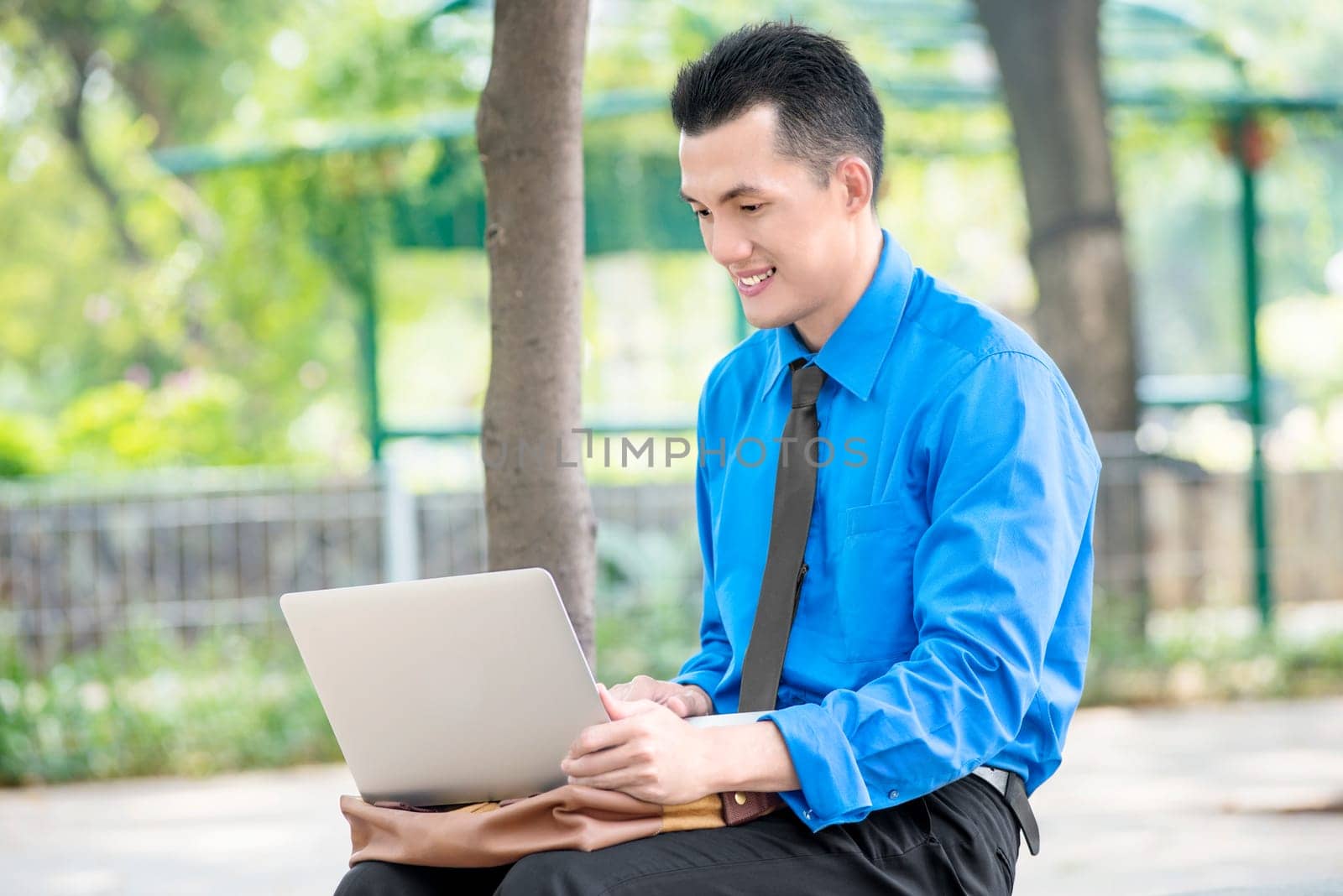 Smiling asian businessman sitting and working with laptop on the park