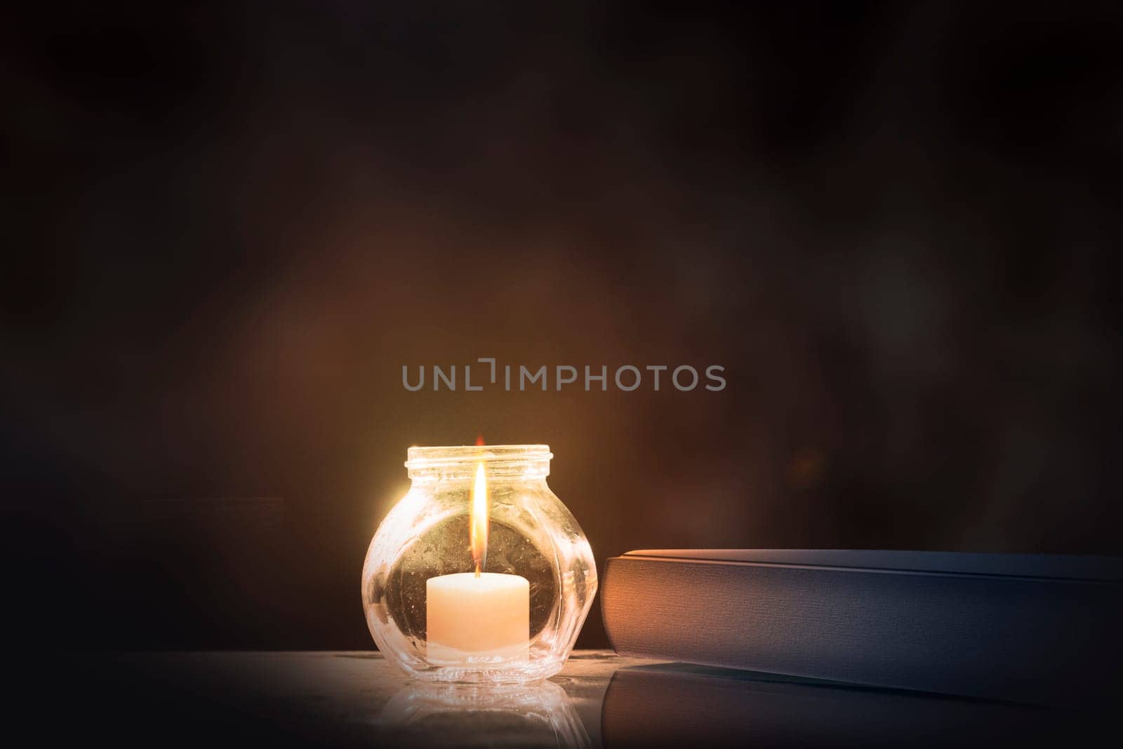 Quran and little candle on wooden table over dark background
