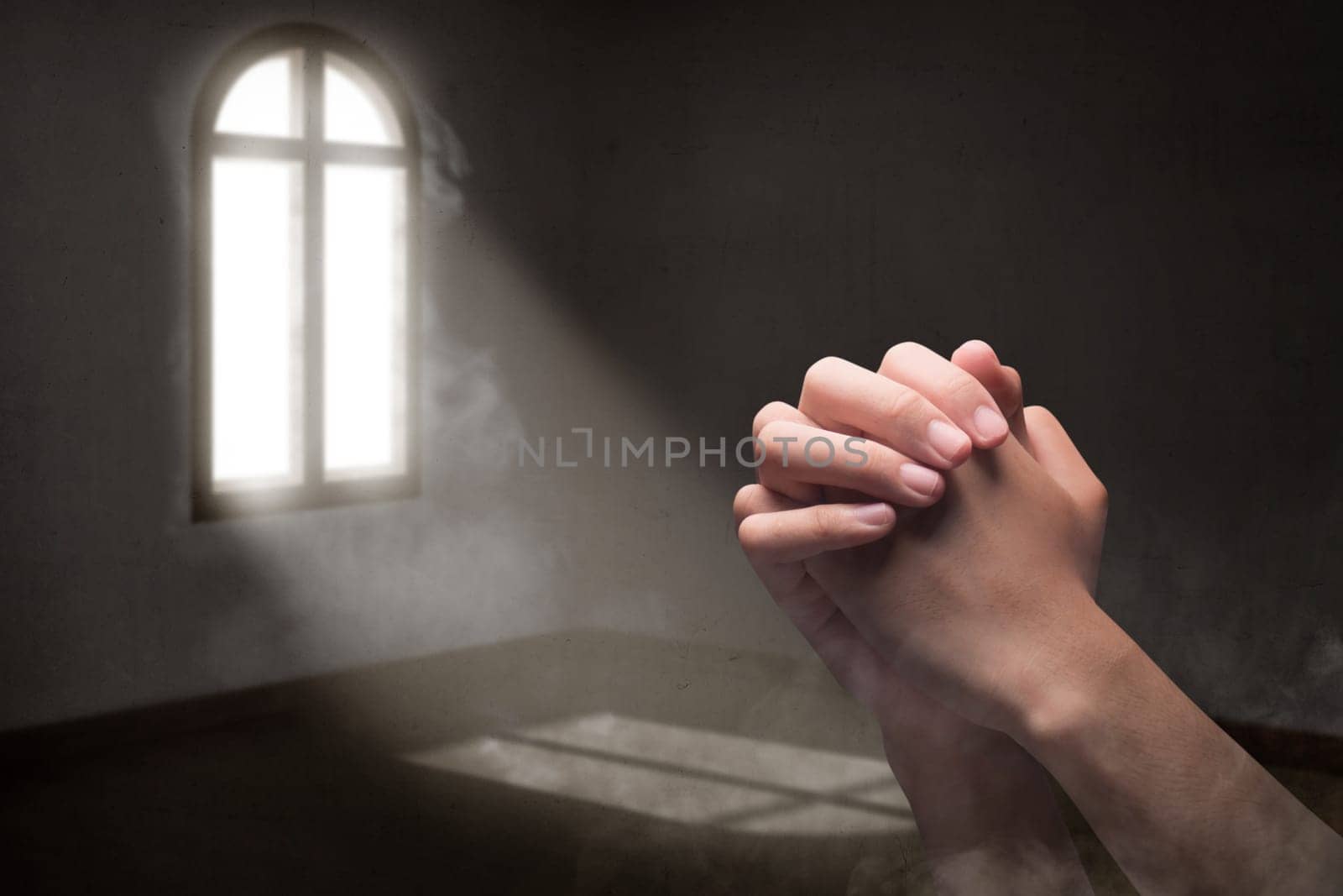 Male hands in praying position inside the room with light from outside the windows