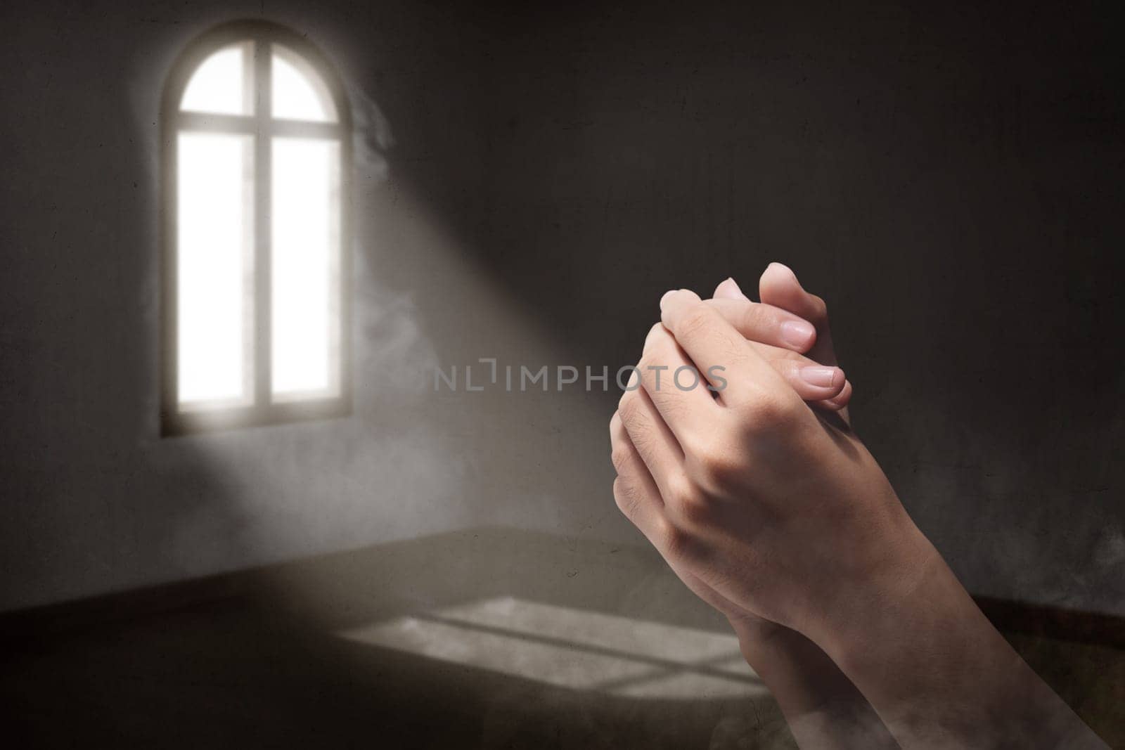 Male hands in praying position inside the room with light from outside the windows
