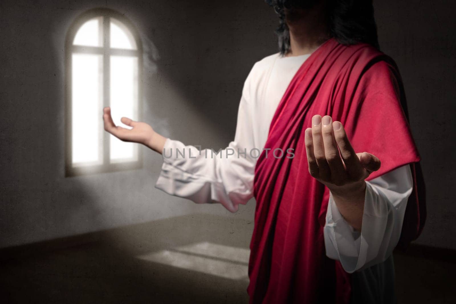 Jesus christ raised hands with open palms and praying to god inside the room with light from outside the windows