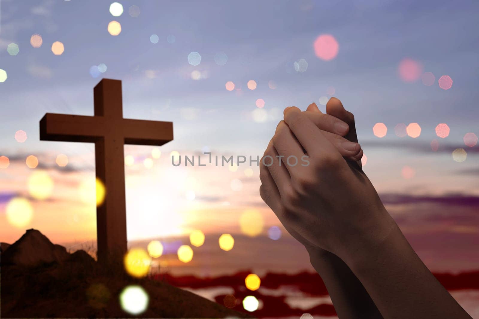 Christian cross and male hands with praying position over sunset background