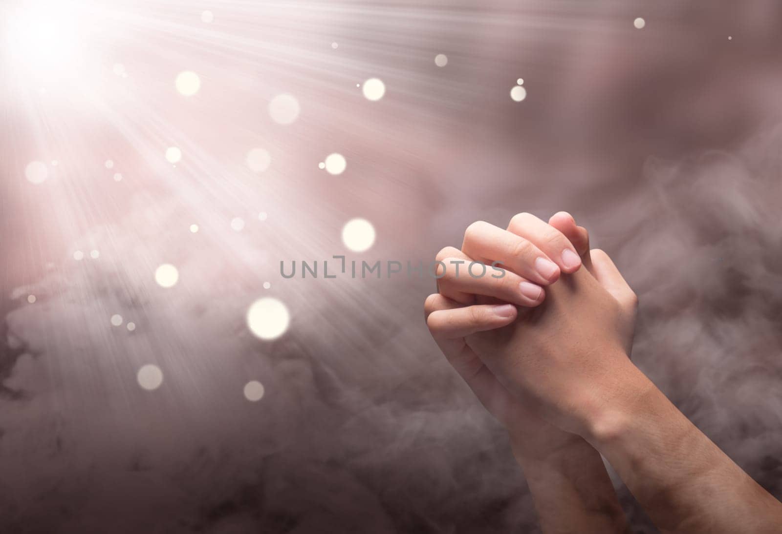 Male hands in praying position with ray over blurry background