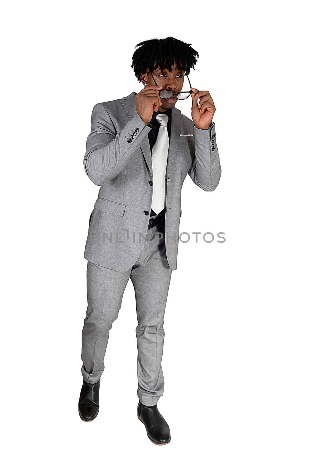 A handsome African American man in a light gray suit putting on his.sunglasses and walking, isolated for white background.