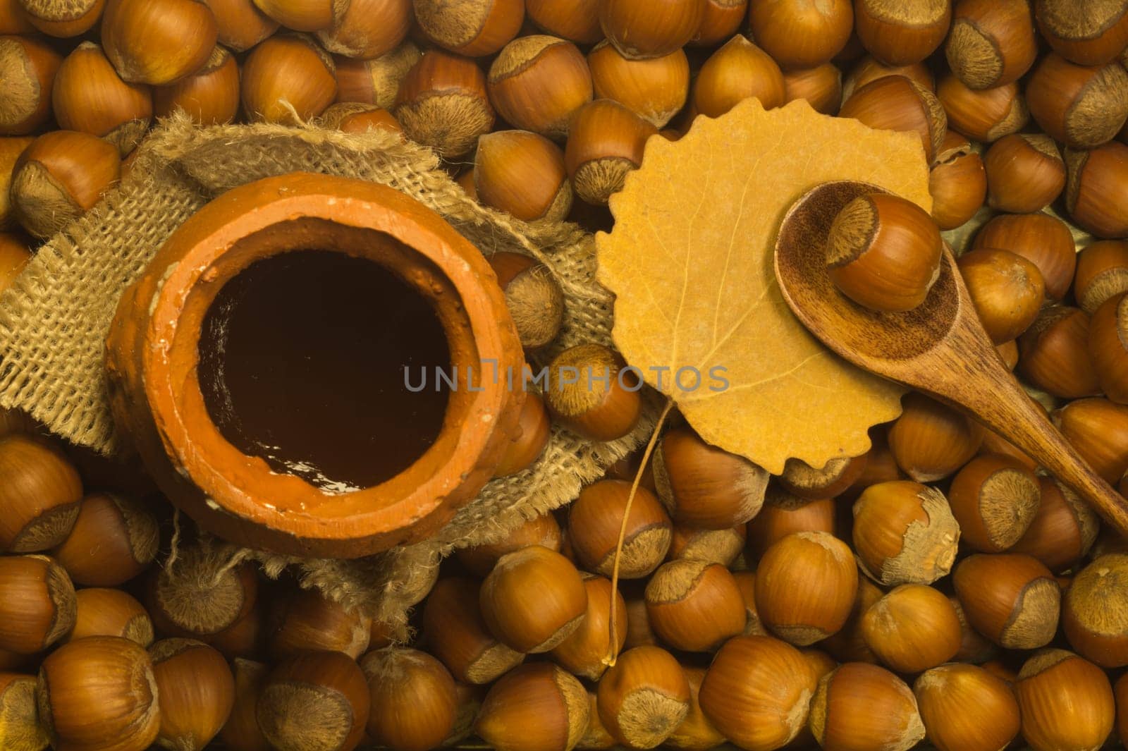 Honey pot with wooden spoon and nuts background