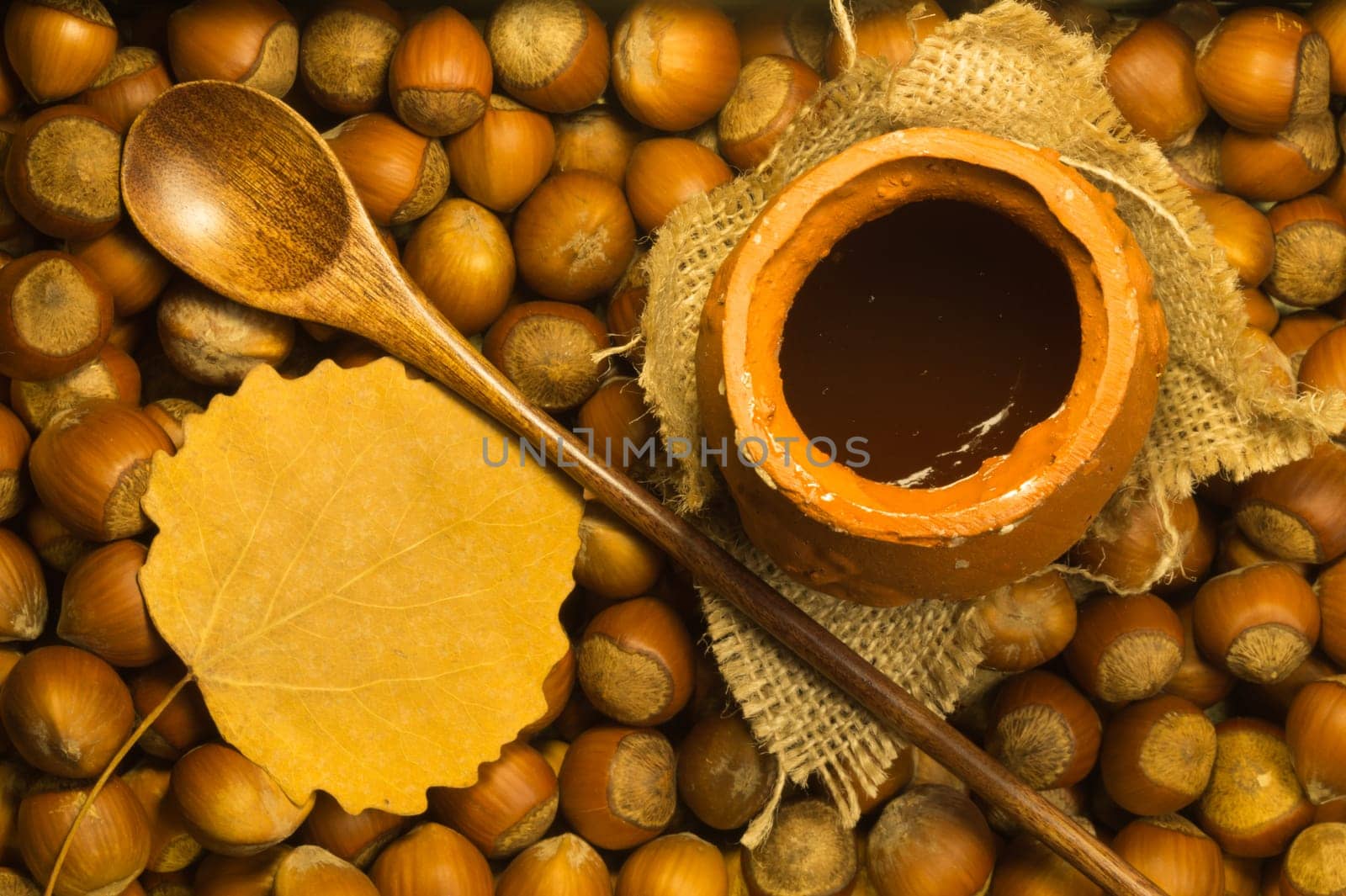 Honey pot with wooden spoon and nuts background