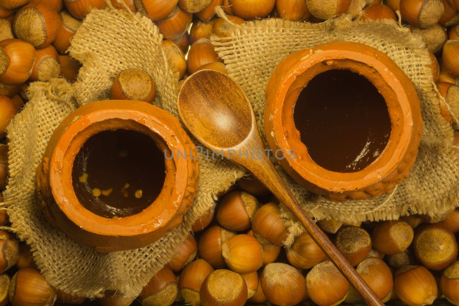 Honey pot with wooden spoon and nuts background