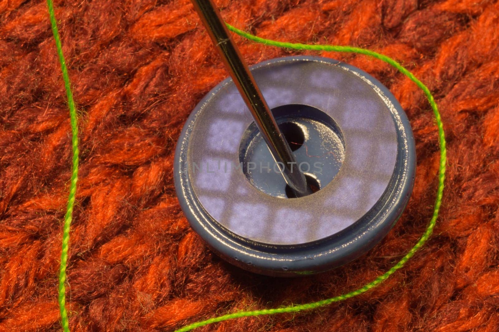Button and needle with thread on red textile background